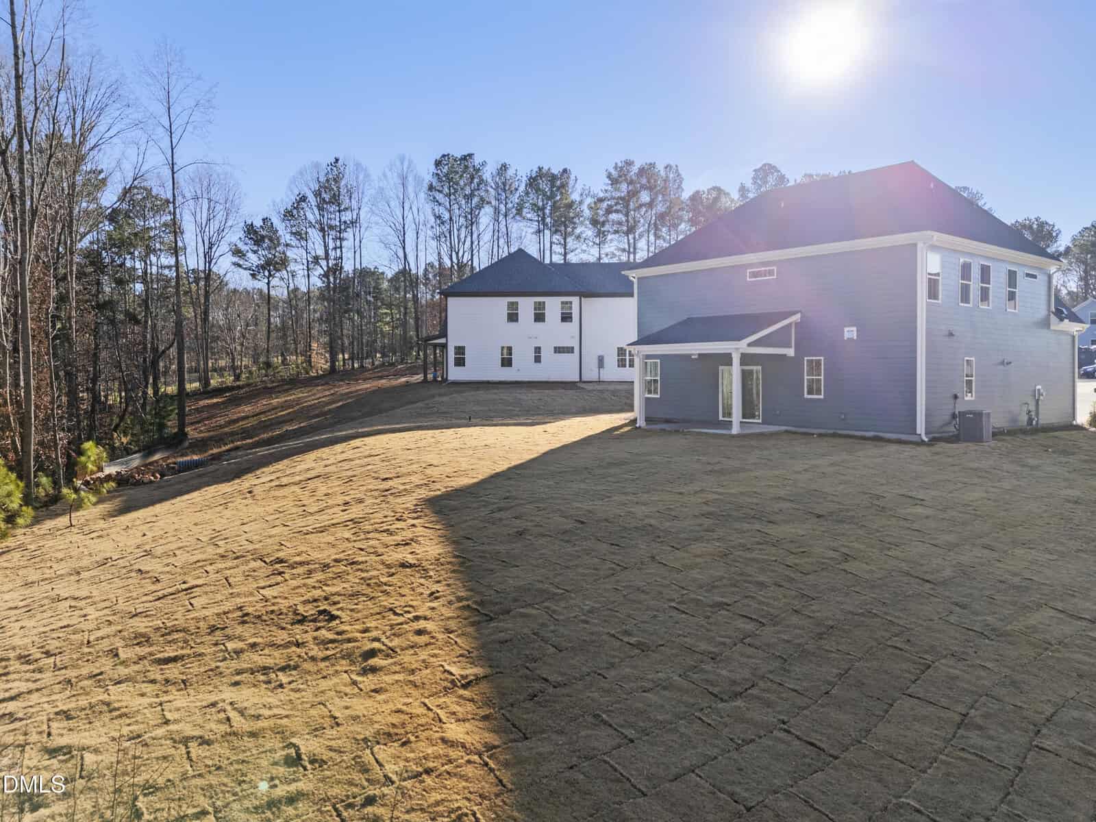 A sunlit backyard with freshly laid sod features two modern two-story houses, one blue and one white, surrounded by trees and a clear blue sky.