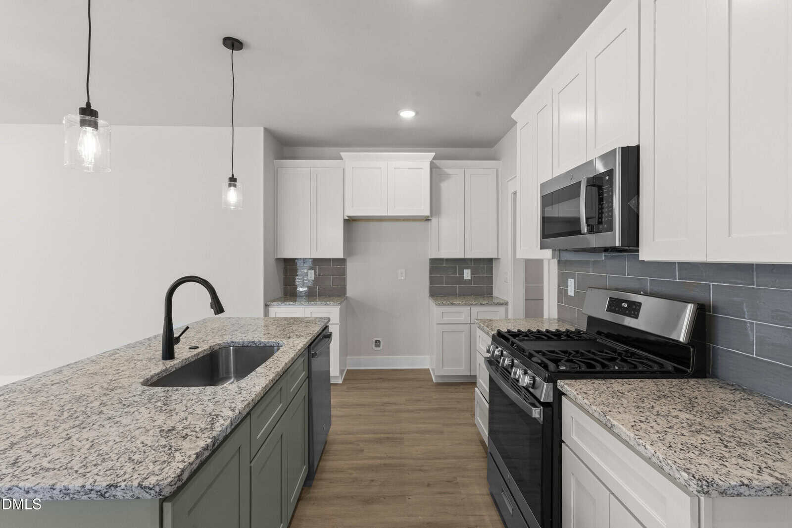 Modern kitchen with white cabinets, granite countertops, a black faucet on the island, stainless steel appliances, gray tile backsplash, wood flooring, and pendant lights hanging above the island.