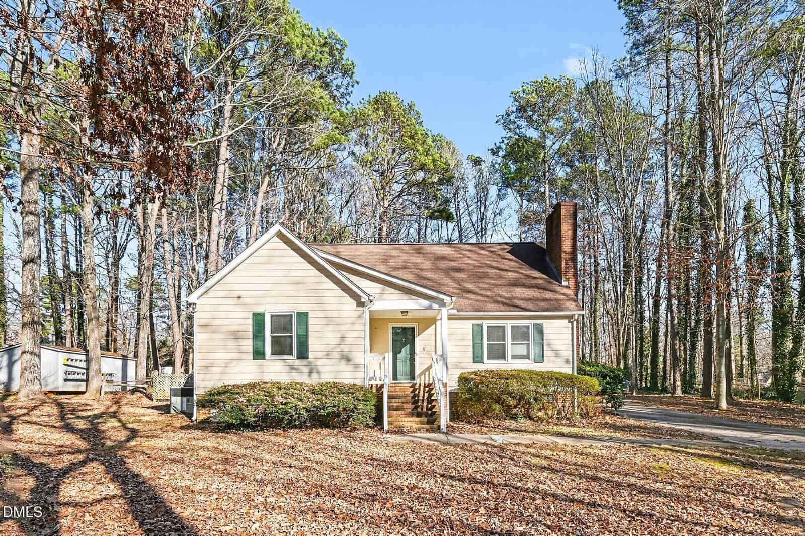 A single-story beige house with a brown roof, white trim, and brick steps sits at 303 S Stratford Drive in Henderson, surrounded by tall trees and fallen leaves. A driveway runs along the right side under a clear blue sky.
