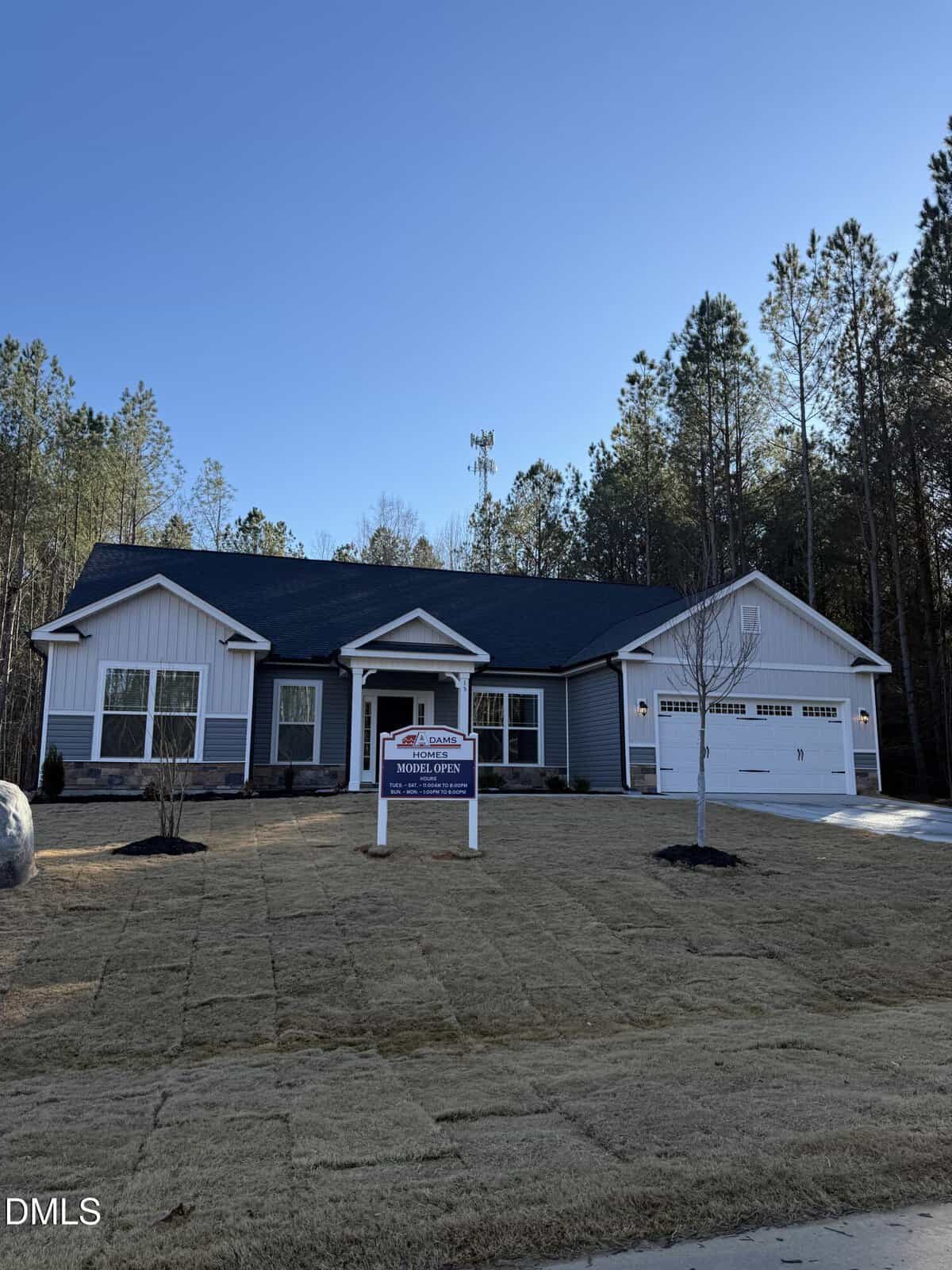 Charming single-story house at 15 Lemon Drop Lane, Franklinton, with gray siding and white trim, a two-car garage, and a "Model Open" sign. The recently sodded lawn is framed by pine trees under a clear blue sky.
