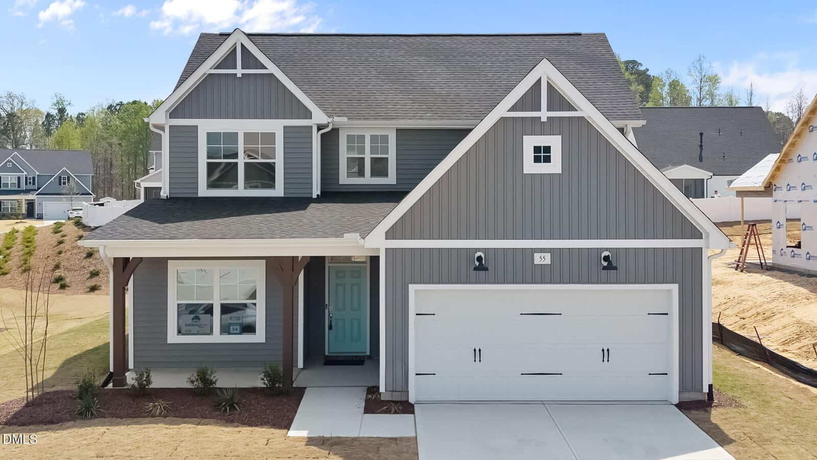 A two-story gray house with white trim, a covered front porch, and a double garage. The lawn is mostly bare with some landscaping near the porch. A neighboring house is partially visible on the right.