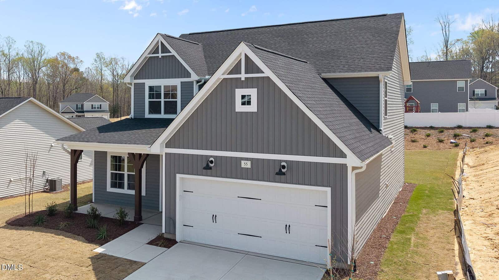 Two-story modern house with gray siding, white trim, a double garage, covered front entry, and landscaped yard. Other houses and trees are visible in the background under a clear sky.