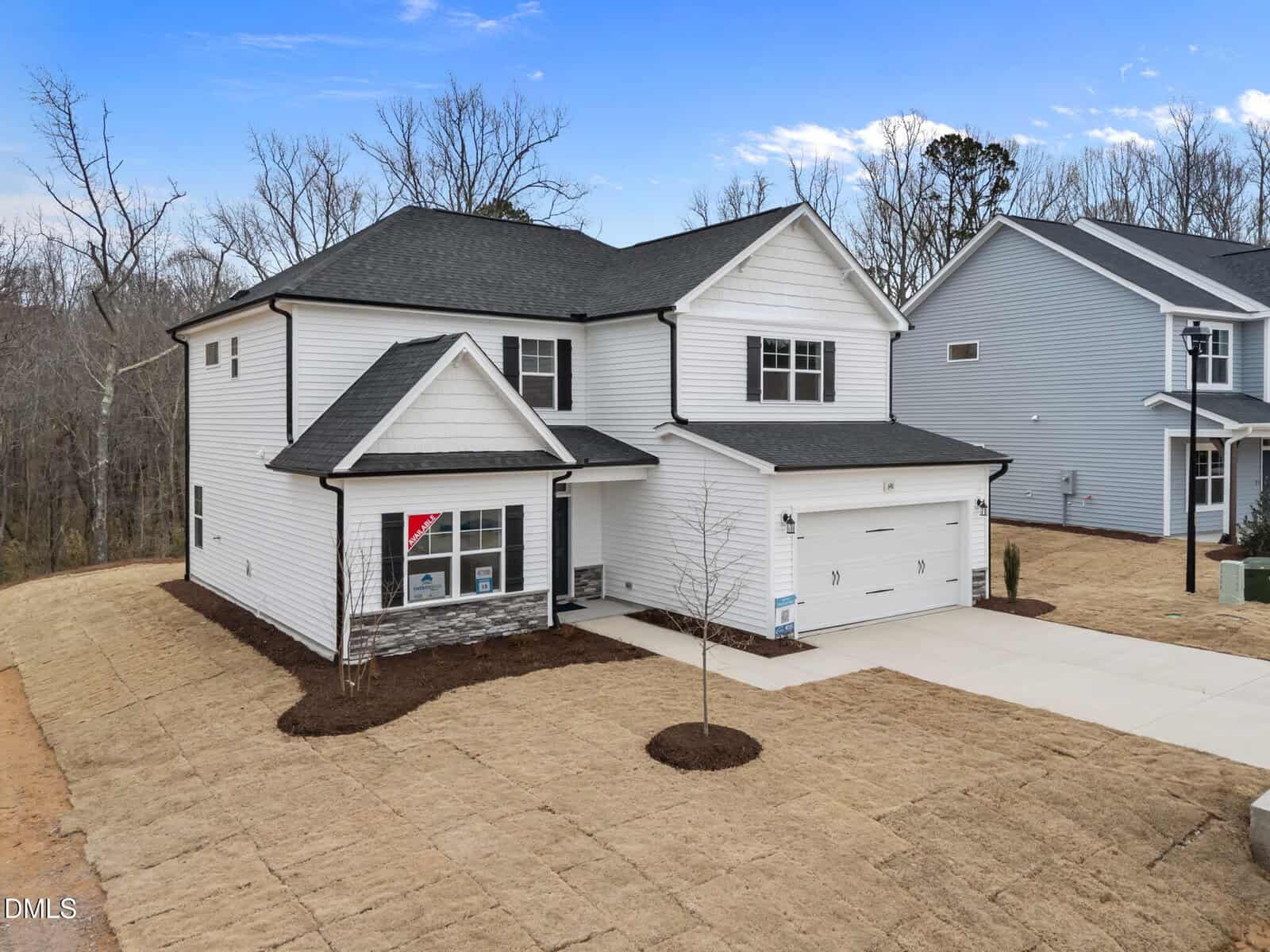 Two-story white house with black roof, two-car garage, and small covered porch. The yard is freshly seeded with straw and a single young tree in front. The house is located in a suburban neighborhood with other similar homes nearby.