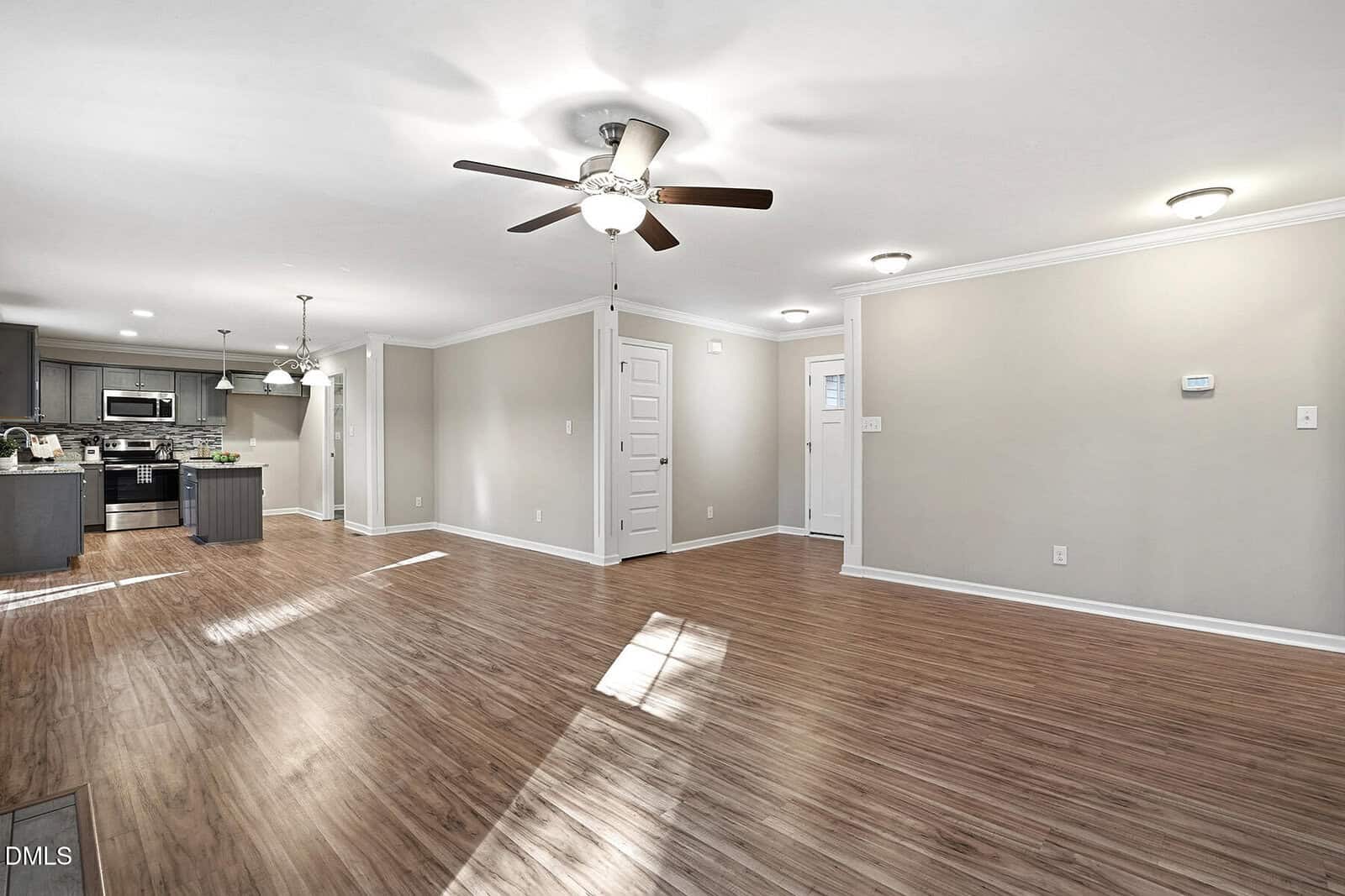 Spacious open-plan living area with wood-style flooring, ceiling fans, recessed lighting, and neutral walls. The area connects to a modern kitchen with stainless steel appliances and an island. Multiple doorways are visible.