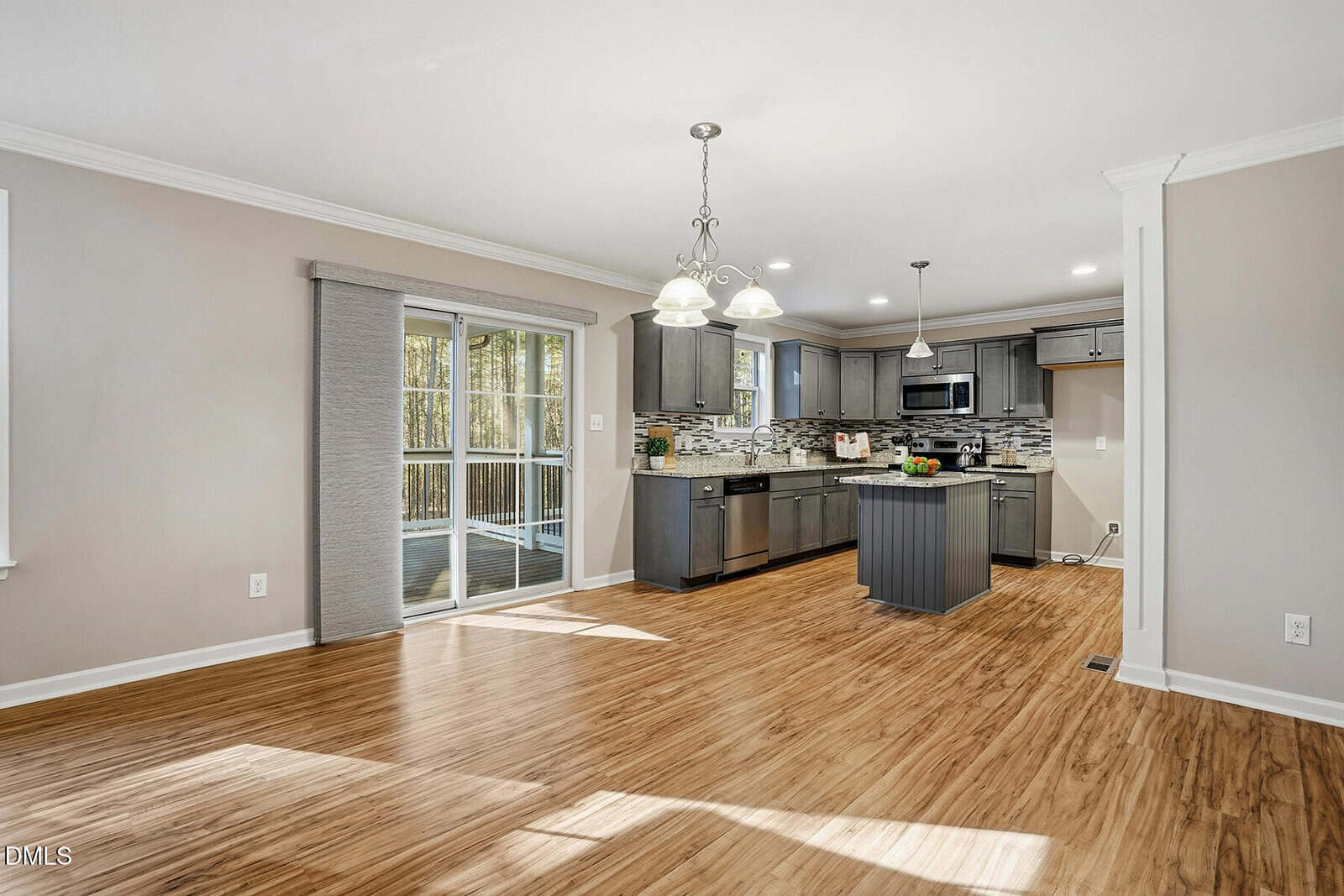 A modern kitchen with stainless steel appliances, gray cabinets, and a tile backsplash opens to a dining area with wood-look flooring and sliding glass doors leading outside.