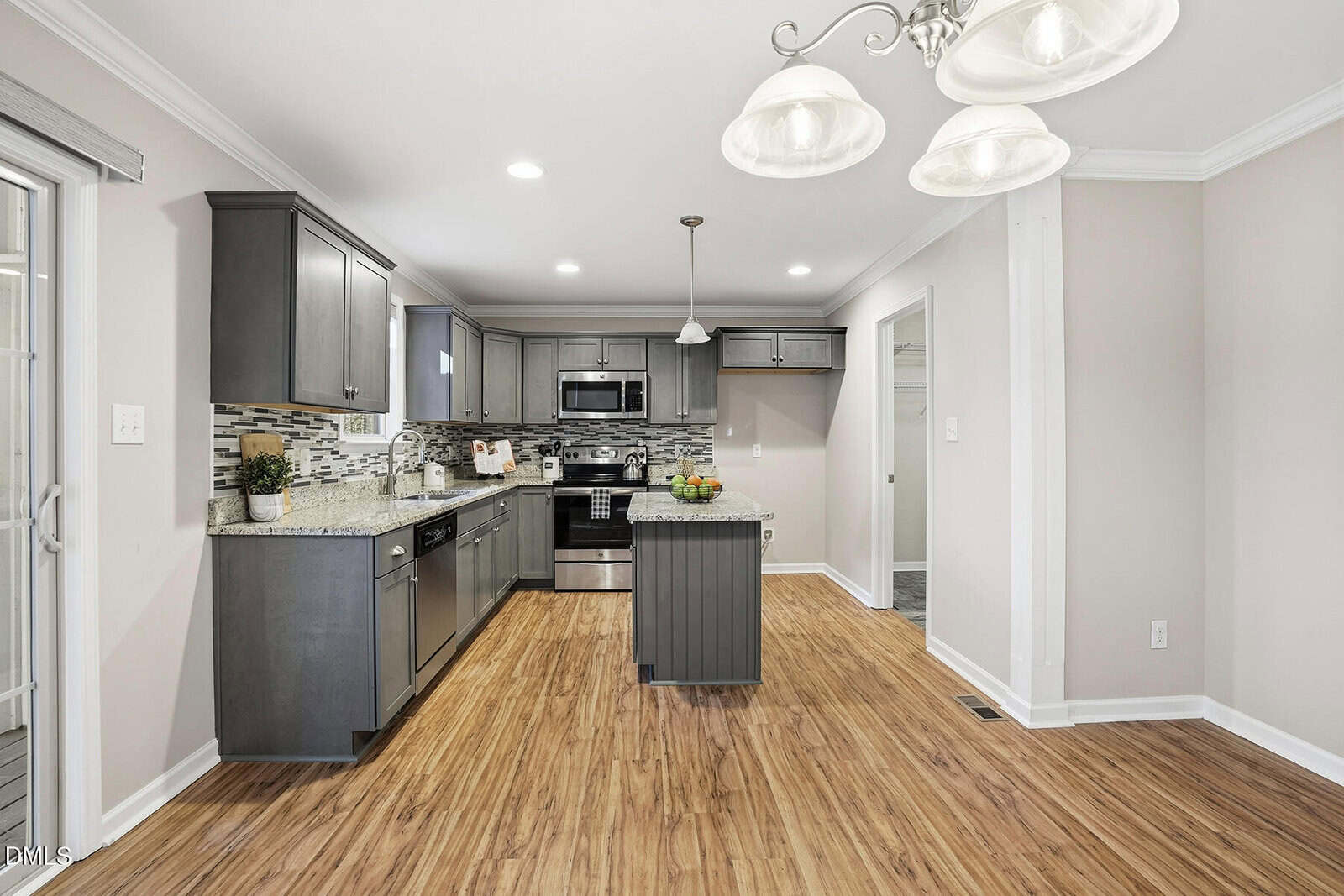 A modern kitchen with gray cabinets, stainless steel appliances, granite countertops, a tile backsplash, wood-style floors, and pendant lighting, opening into a dining area with a light fixture and neutral walls.