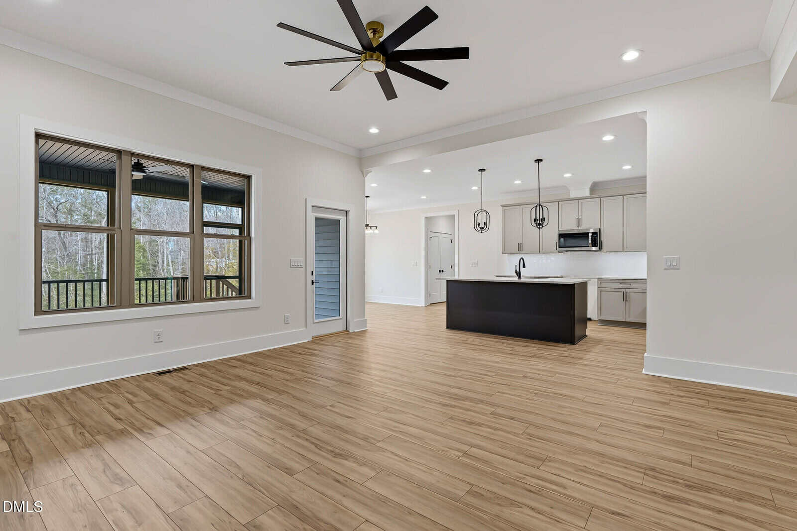 Open-plan living space with wood-style flooring, large windows, ceiling fan, and recessed lighting. Kitchen features white cabinets, a black island, pendant lights, and stainless steel appliances. Door leads to a covered porch.