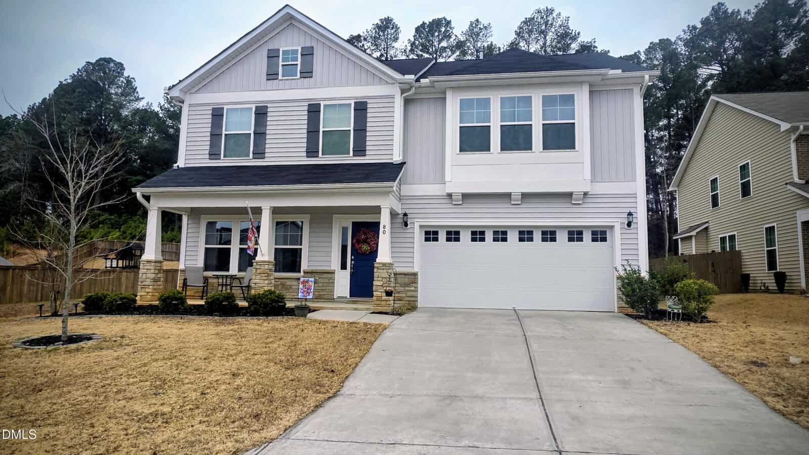 A two-story suburban house at 80 Wolverton Way in Franklinton with white siding, black shutters, a columned front porch, and a double garage. The yard features sparse yellow grass and a concrete driveway, with trees and neighbors nearby.