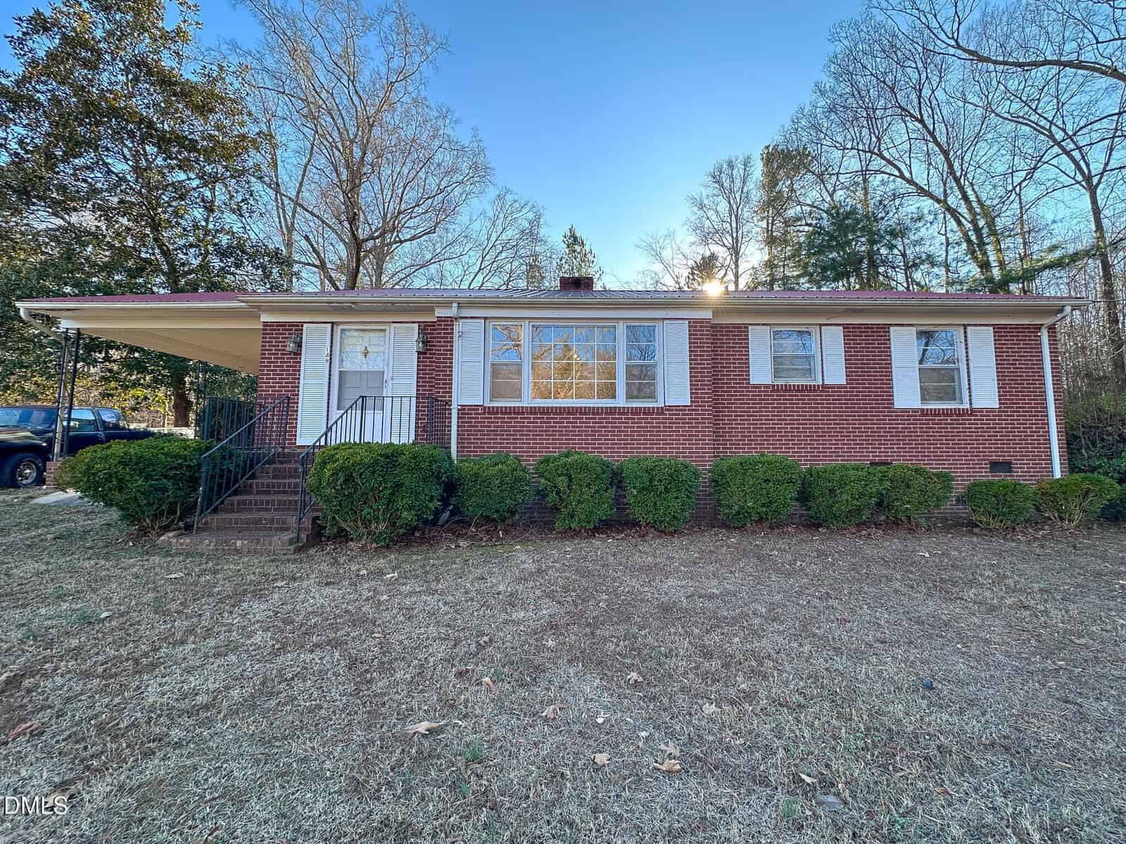 Charming single-story red brick house in Warrenton with white shutters and trim, front steps leading to a door with a metal railing, hedges along the house, bare trees in the background, and a mostly clear blue sky at 149 Ridgecrest Drive.
