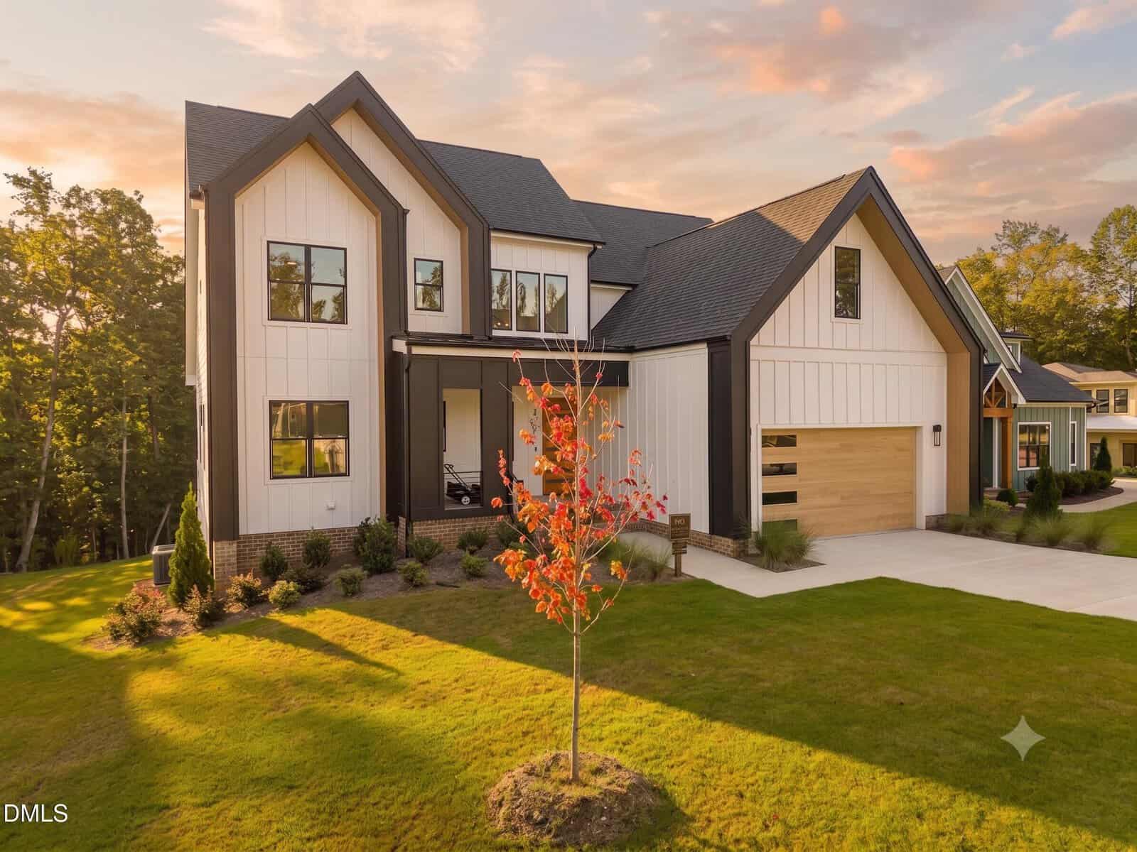 Modern two-story house with white vertical siding, black trim, and a two-car garage at 205 Red Cardinal Court in Youngsville. A young tree with red leaves is planted in the front yard. The sky is partly cloudy with a warm sunset glow.