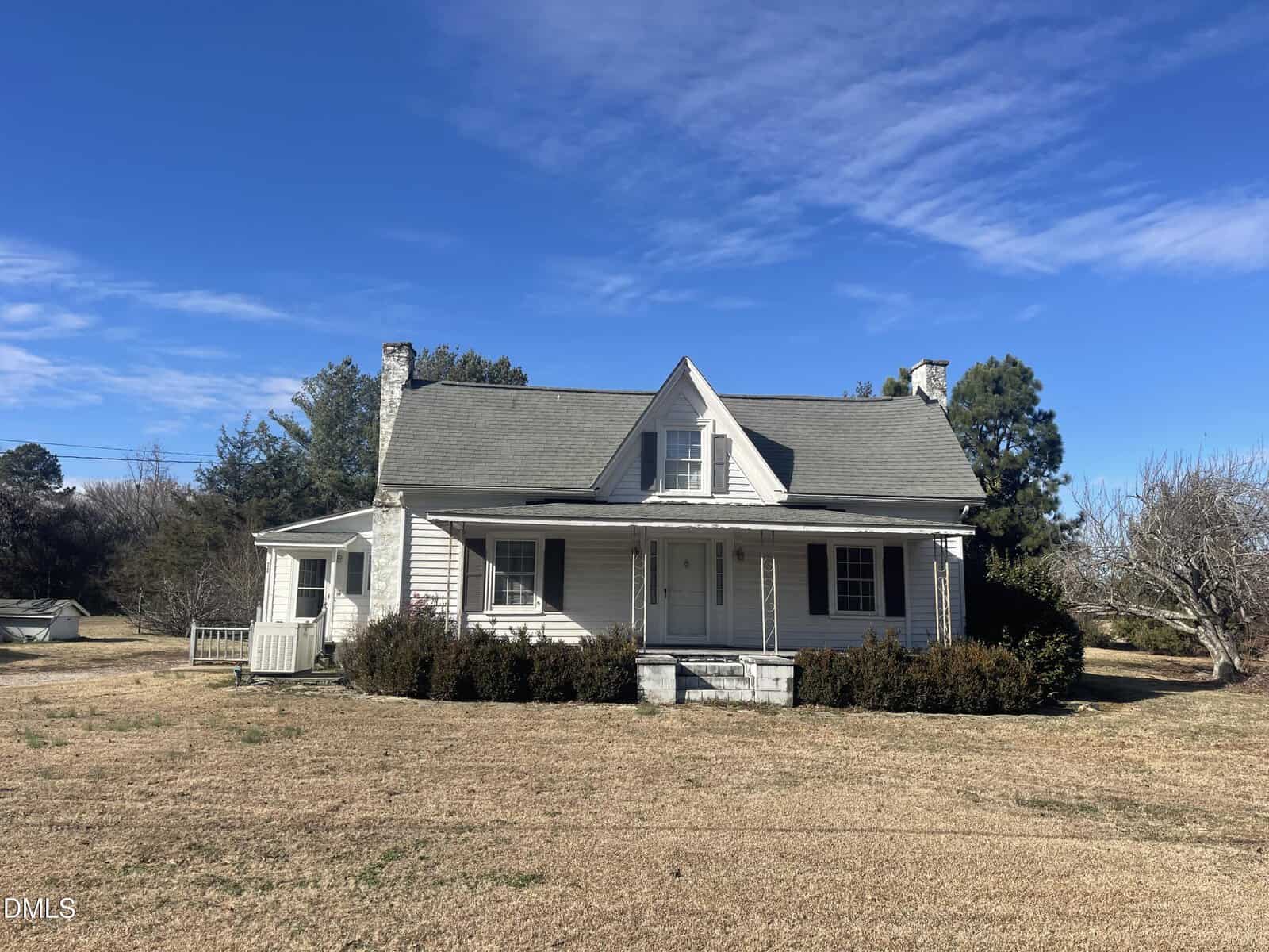 A small, white, two-story house with a front porch and dormer window sits in a large, grassy yard at 1116 New Bethel Church Road in Henderson. Bushes line the front of the house under a blue sky with scattered clouds.