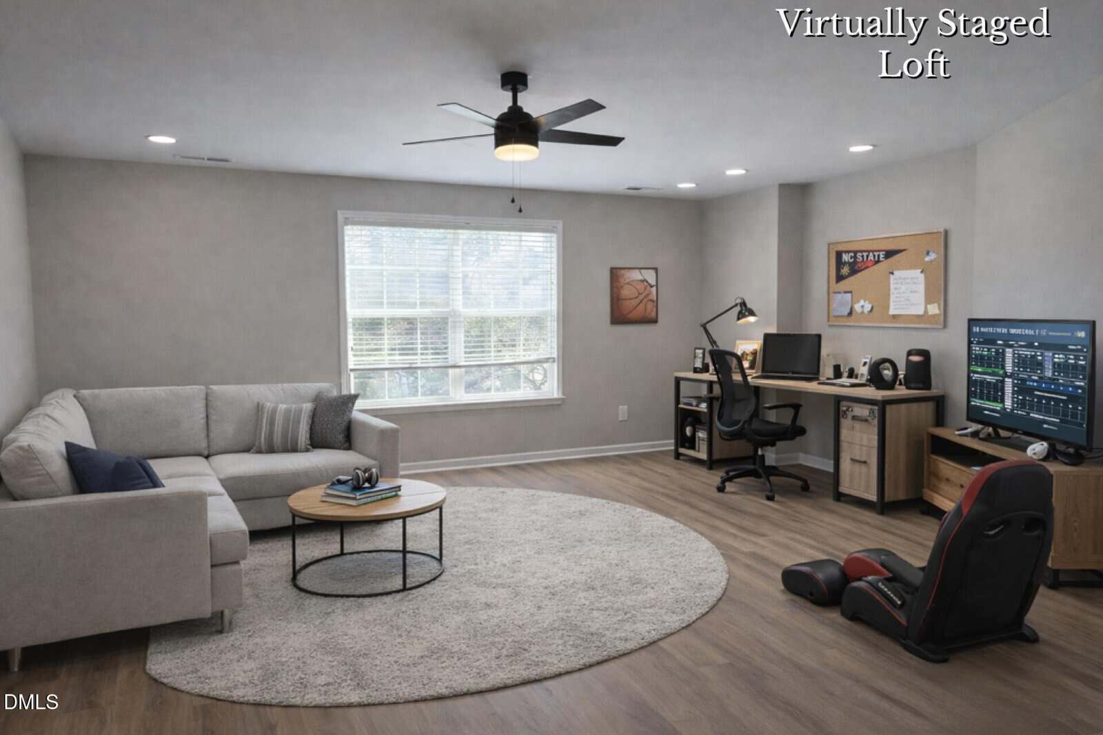 A modern loft with wood flooring features a sectional sofa, round coffee table, and soft rug. A desk with a computer setup sits in the corner, and a gaming chair faces a TV. Large window lets in natural light. Text reads "Virtually Staged Loft.