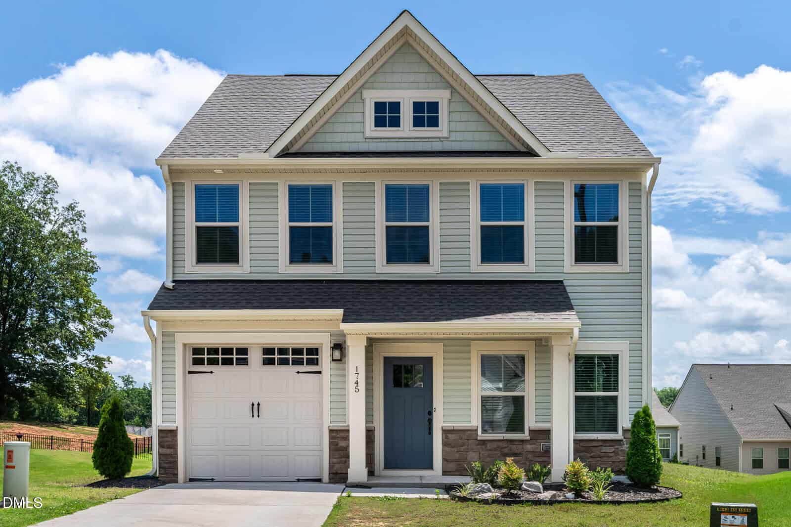 Two-story suburban house with gray siding, white trim, and a single-car garage located at 1745 Ripley Woods Street in Wake Forest. The front door is gray, and there are five upper windows. The house sits on a small lawn with bushes and a concrete driveway.