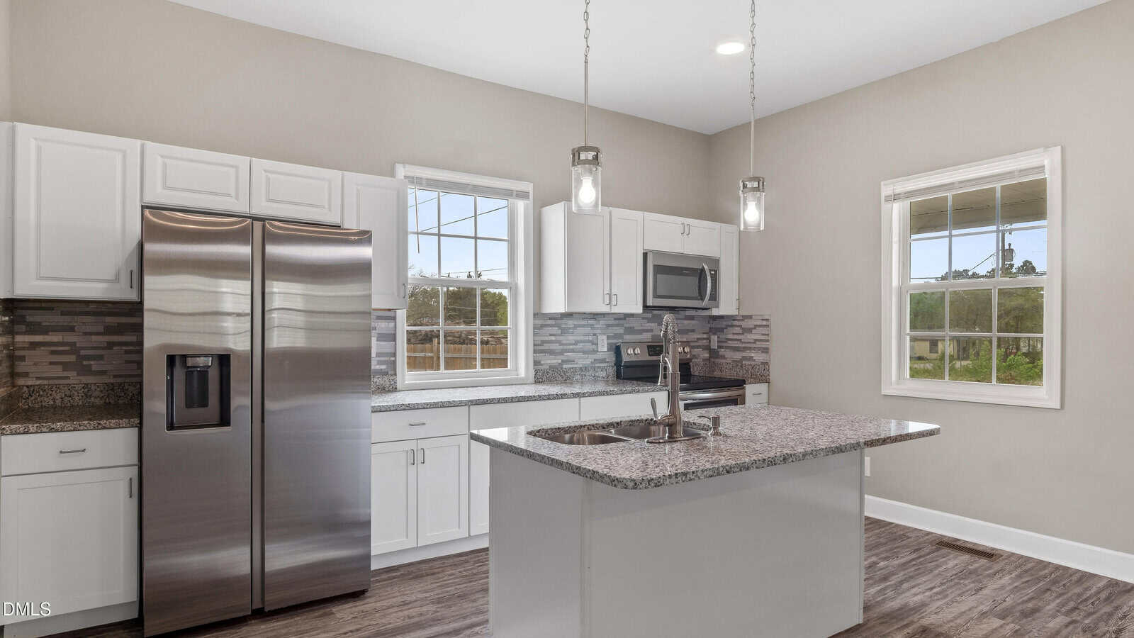Modern kitchen with stainless steel appliances, white cabinets, granite countertops, a center island with a sink, pendant lighting, and large windows letting in natural light.
