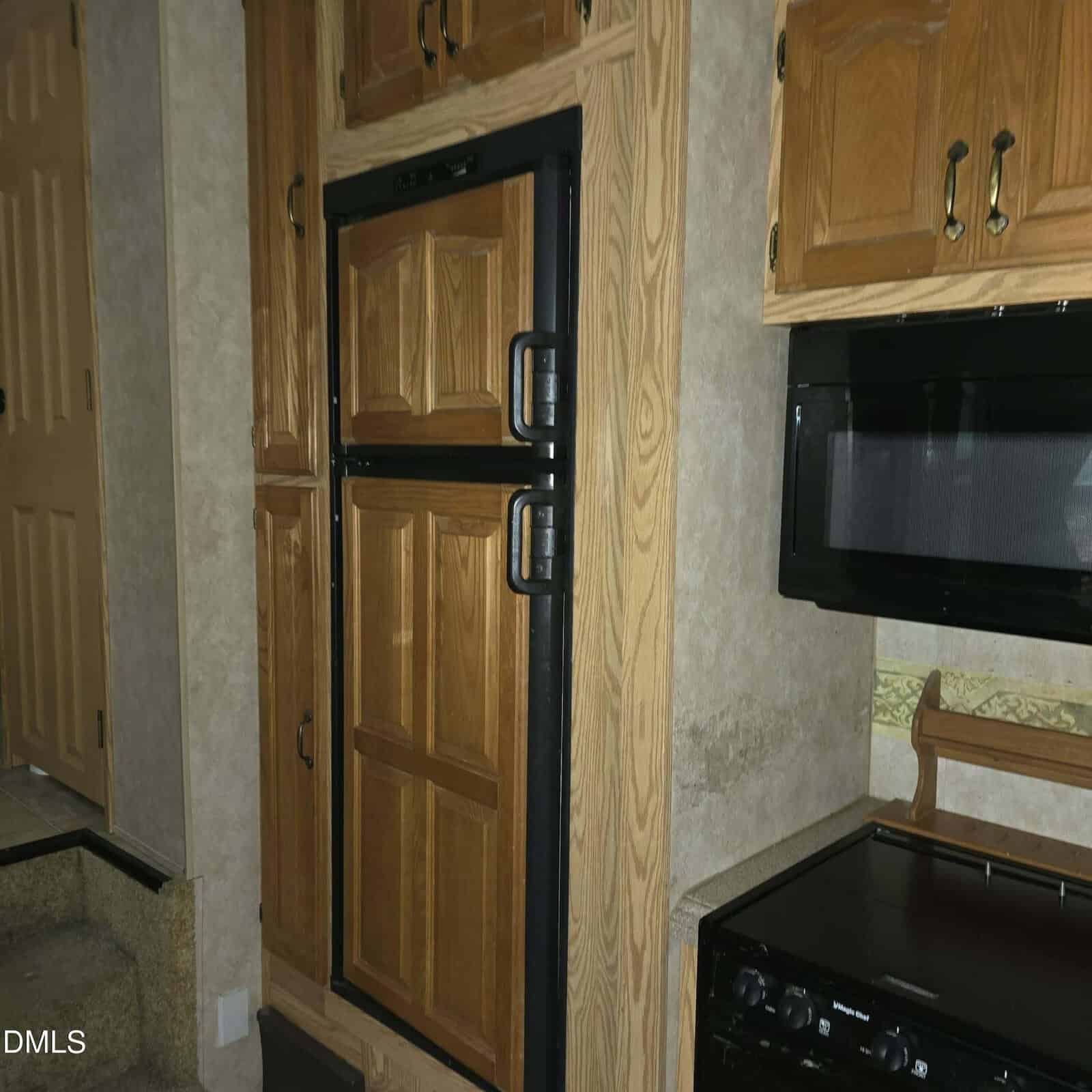 A kitchen area with wood-paneled cabinets and a matching wood-paneled refrigerator, black stove, and microwave. Stairs are visible on the left side of the image.