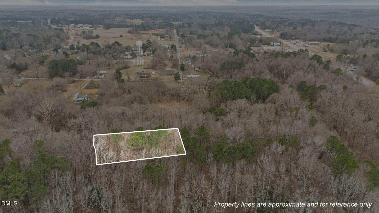 Aerial view of a wooded area with a rectangular plot outlined in white, surrounded by trees, with a rural town, water towers, and roads visible in the background. Text reads, "Property lines are approximate and for reference only.