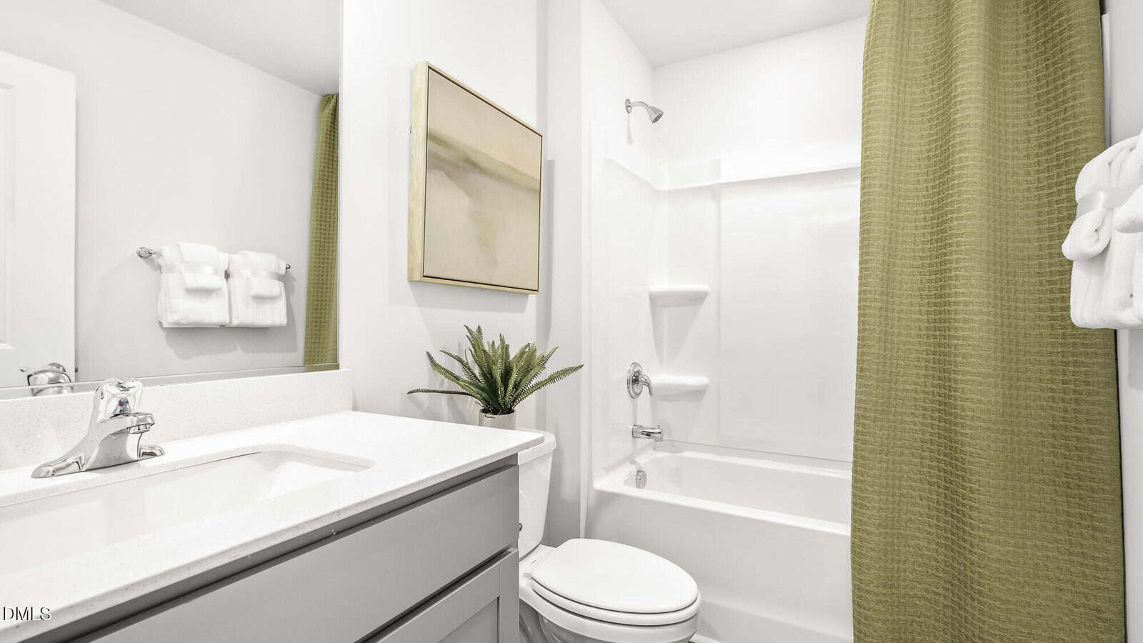 A modern white bathroom with a sink, toilet, tub-shower combo, greenish-yellow shower curtain, white countertop, mirror, wall art, plant, and towels.