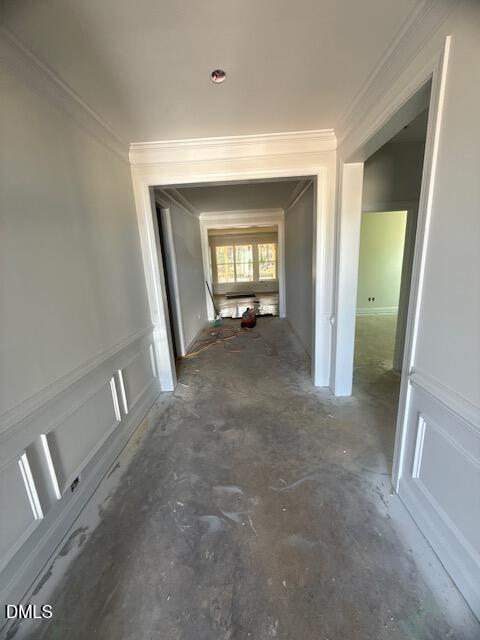 A hallway in a house under construction with unfinished floors, white walls, open doorways on each side, and construction materials scattered on the floor. Sunlight enters through windows at the far end.