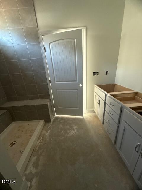 A bathroom under construction with bare floors, grey tiled shower, grey door, and unfinished vanity cabinets without countertops or sinks.