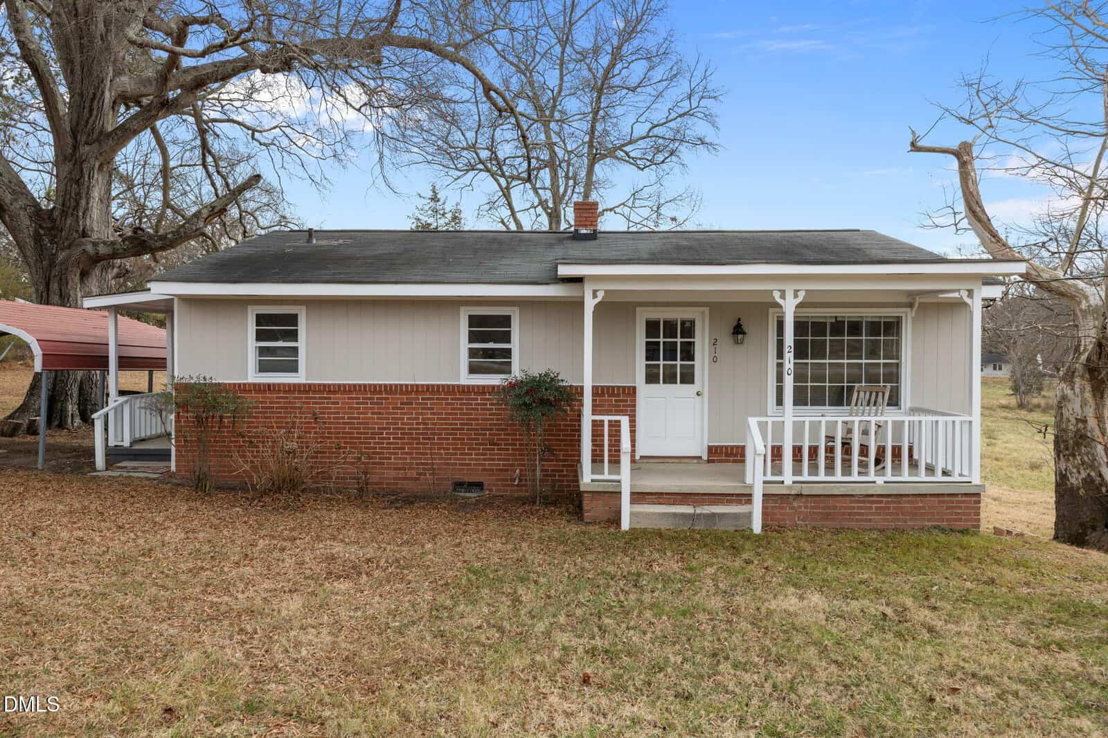Charming single-story house at 210 E Green Street, Franklinton, featuring a front porch, brick lower half, light-colored upper siding, white trim, steps to the entrance, and large bare trees in the yard under a blue sky.