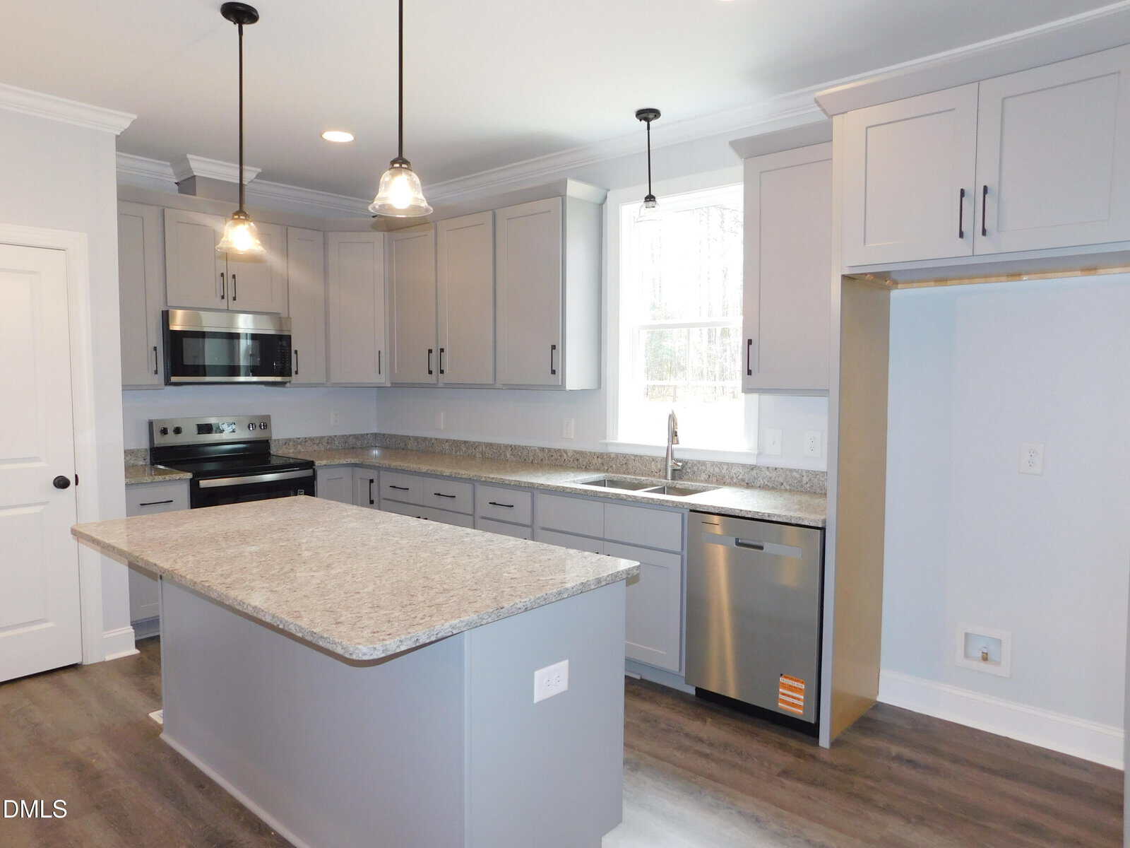 Modern kitchen with gray cabinets, granite countertops, stainless steel appliances, an island with outlets, pendant lights, and wood-look flooring. There is an empty space likely intended for a refrigerator on the right side.