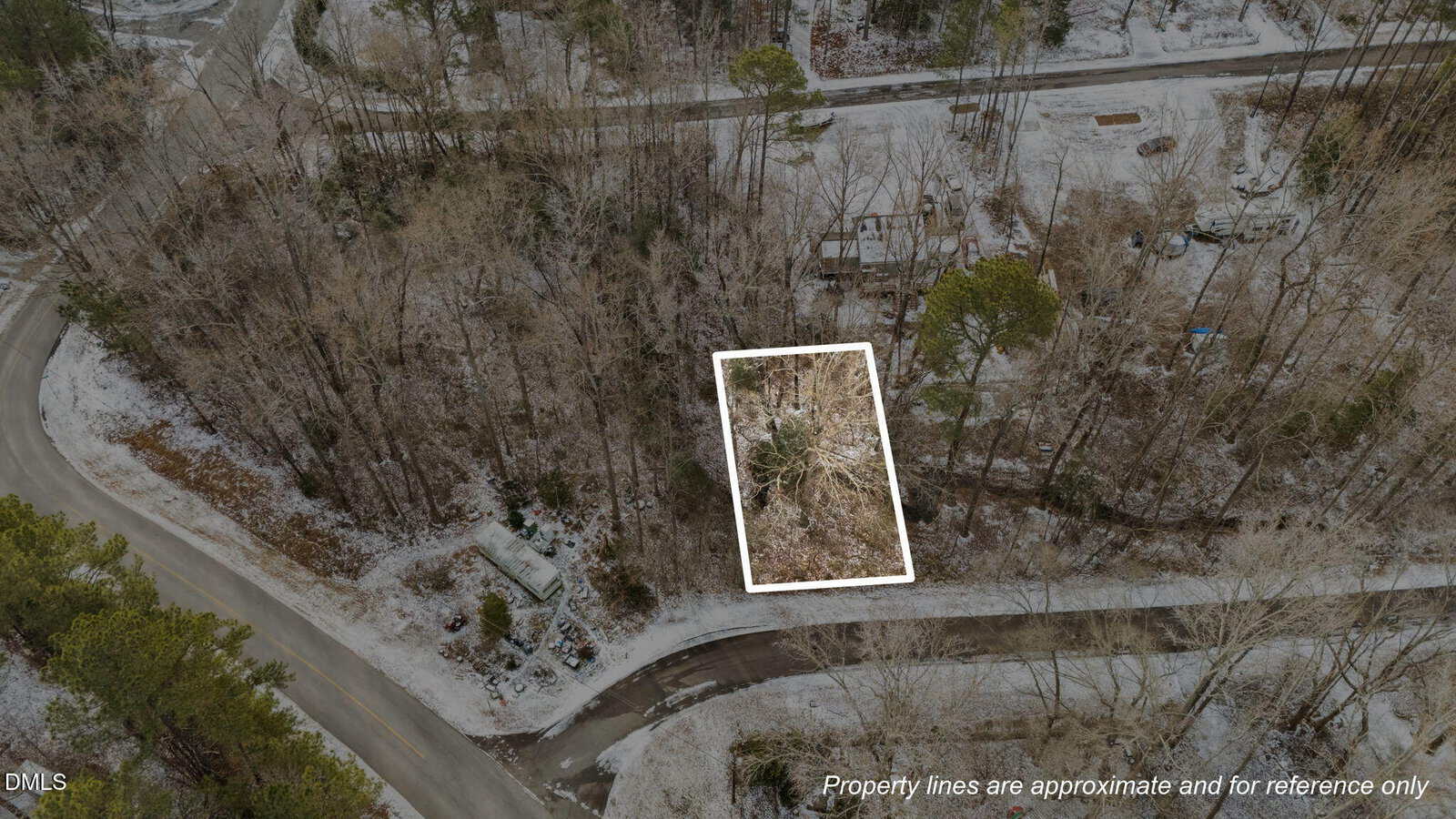Aerial view of a rectangular, wooded lot outlined in white, located between curving roads in a sparsely wooded area with light snow covering the ground. Text at bottom notes property lines are approximate.