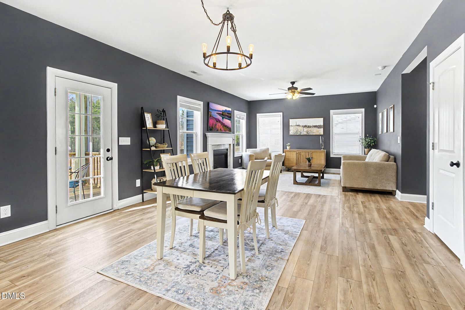 Open-concept living and dining area with gray walls, light wood floors, a rectangular dining table with six chairs, a chandelier, sofa, coffee table, and large windows letting in natural light.