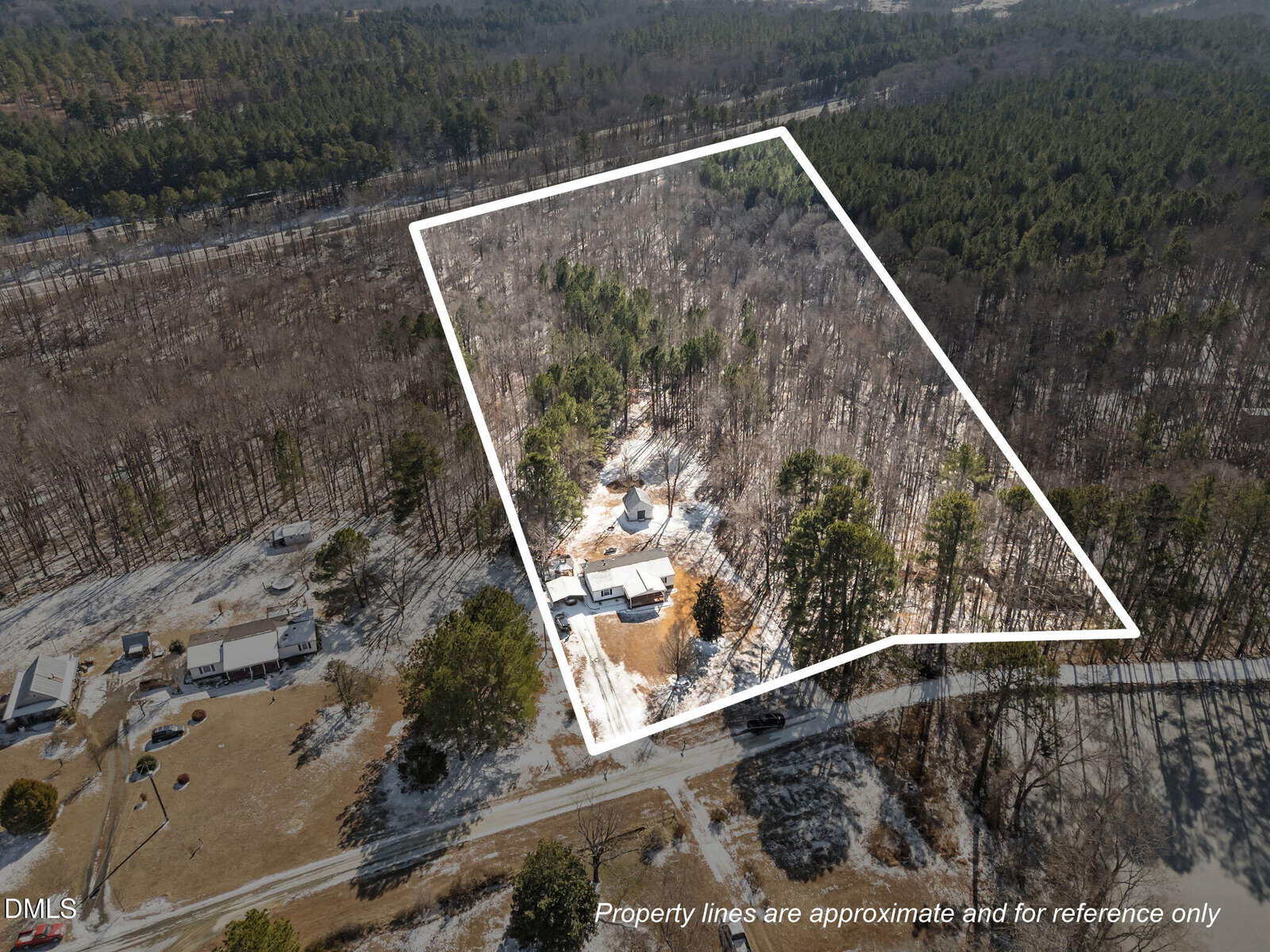 Aerial view of a snow-dusted, wooded property with approximate boundary lines marked in white. The property includes a house and other structures nestled among trees. Text at bottom states boundaries are for reference only.