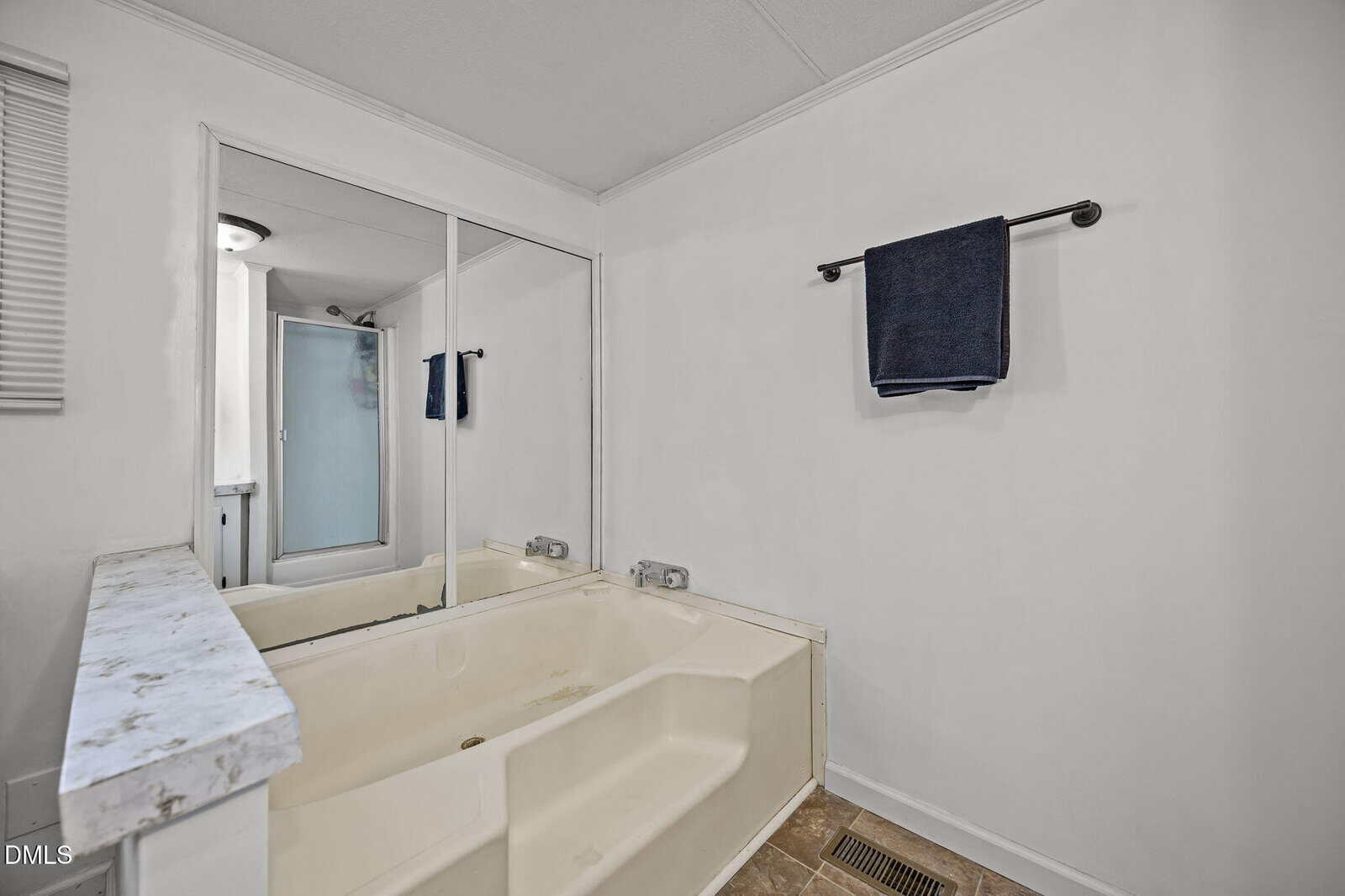 A bathroom with a large beige soaking tub, a marble ledge, a towel bar with a dark towel, and a mirrored wall. A shower with a glass door is visible in the background.