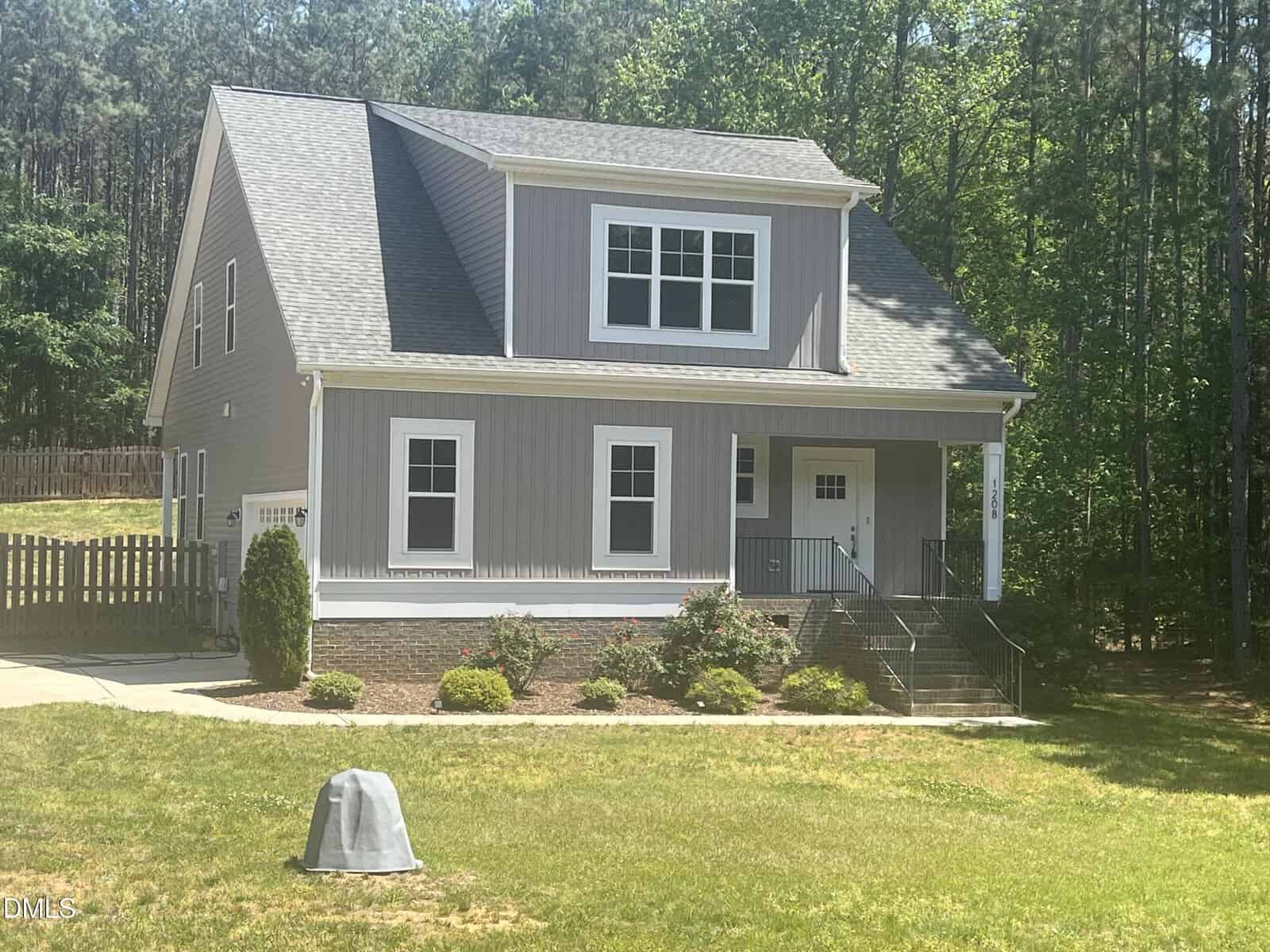A two-story gray house with white trim at 1208 Montgomery Road in Franklinton features a covered front porch, steps leading to the entrance, and is surrounded by a grassy yard, landscaping, and trees in the background.