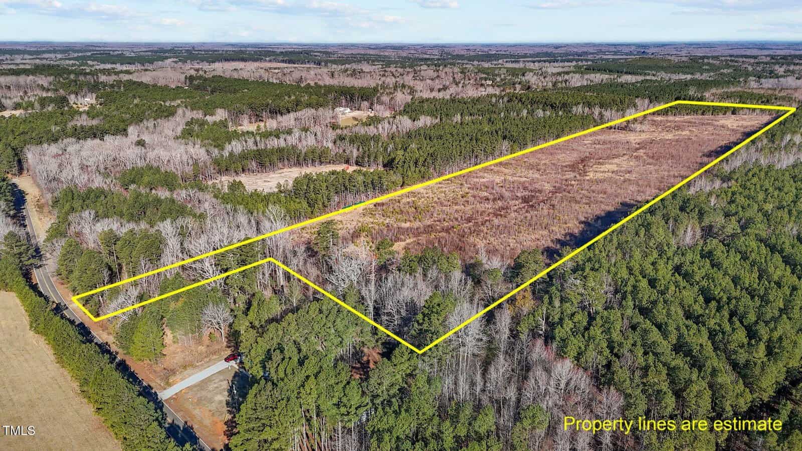 Aerial view of a large, wooded rural area with a long, rectangular section outlined in yellow, indicating estimated property boundaries; a road runs along the left side of the property.