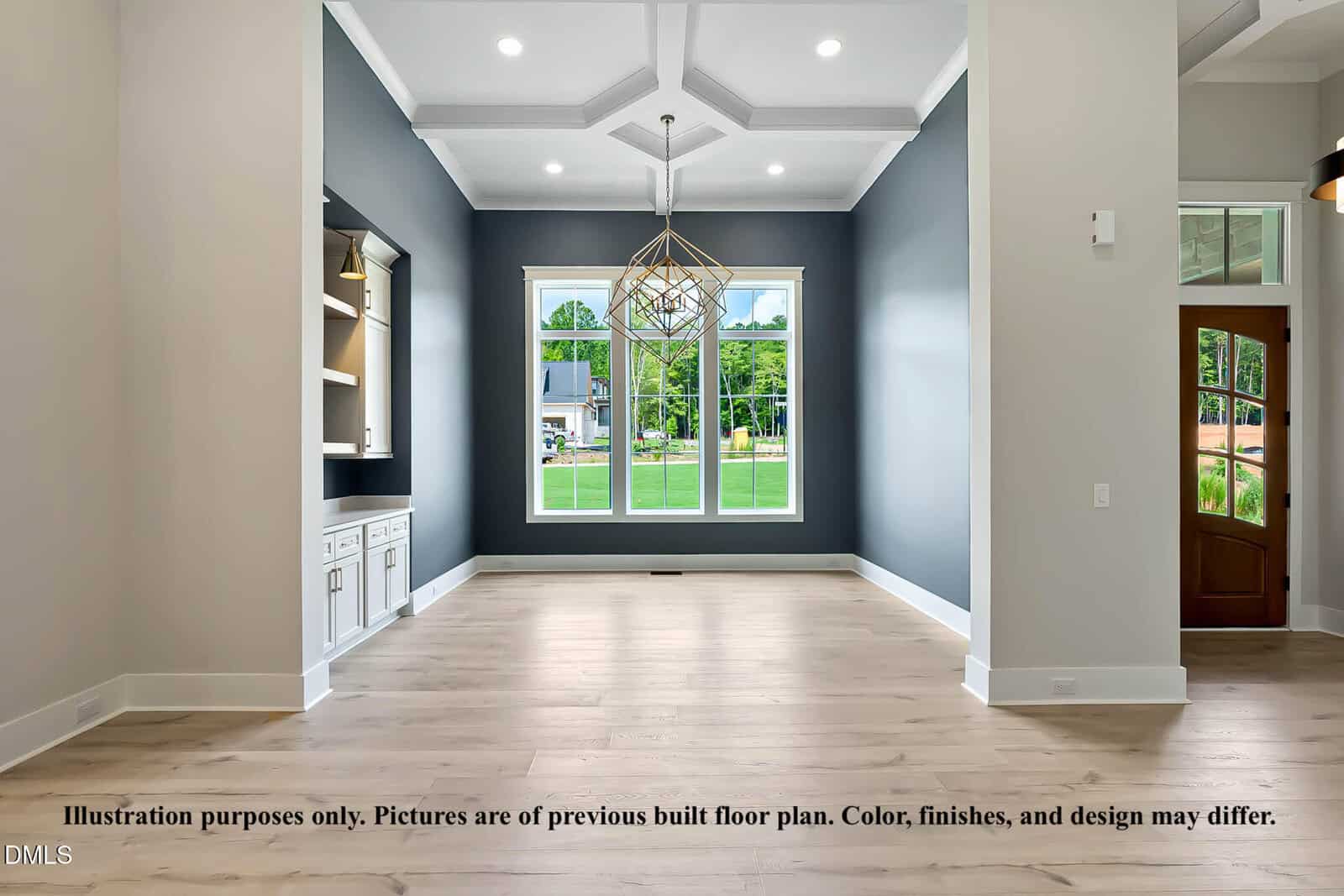A modern, unfurnished dining room with light wood floors, dark accent walls, built-in shelving, large windows facing a green yard, coffered ceiling, and a geometric chandelier.