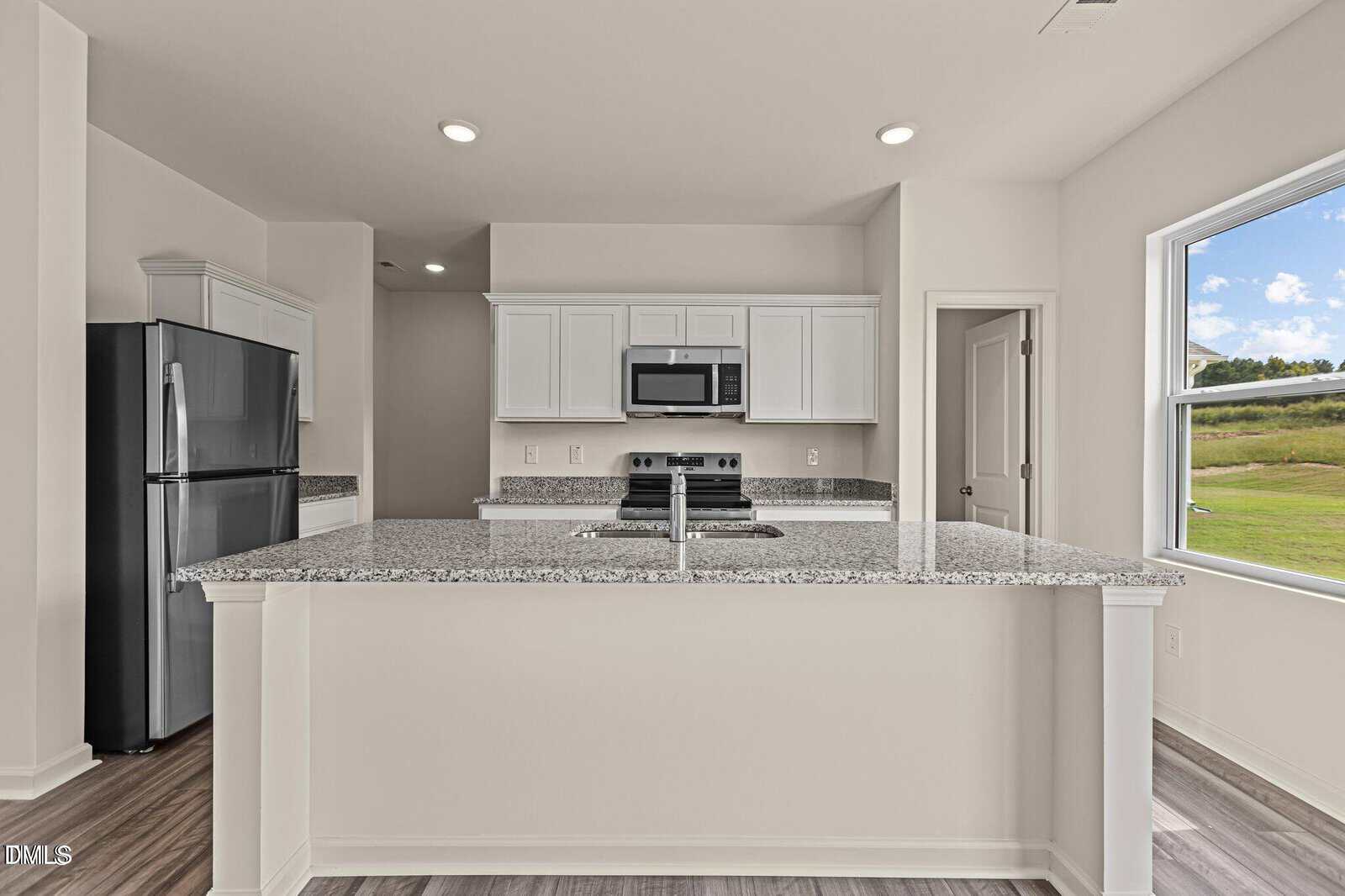 Modern kitchen with white cabinets, granite countertops, stainless steel appliances, and a large window overlooking a grassy outdoor area.
