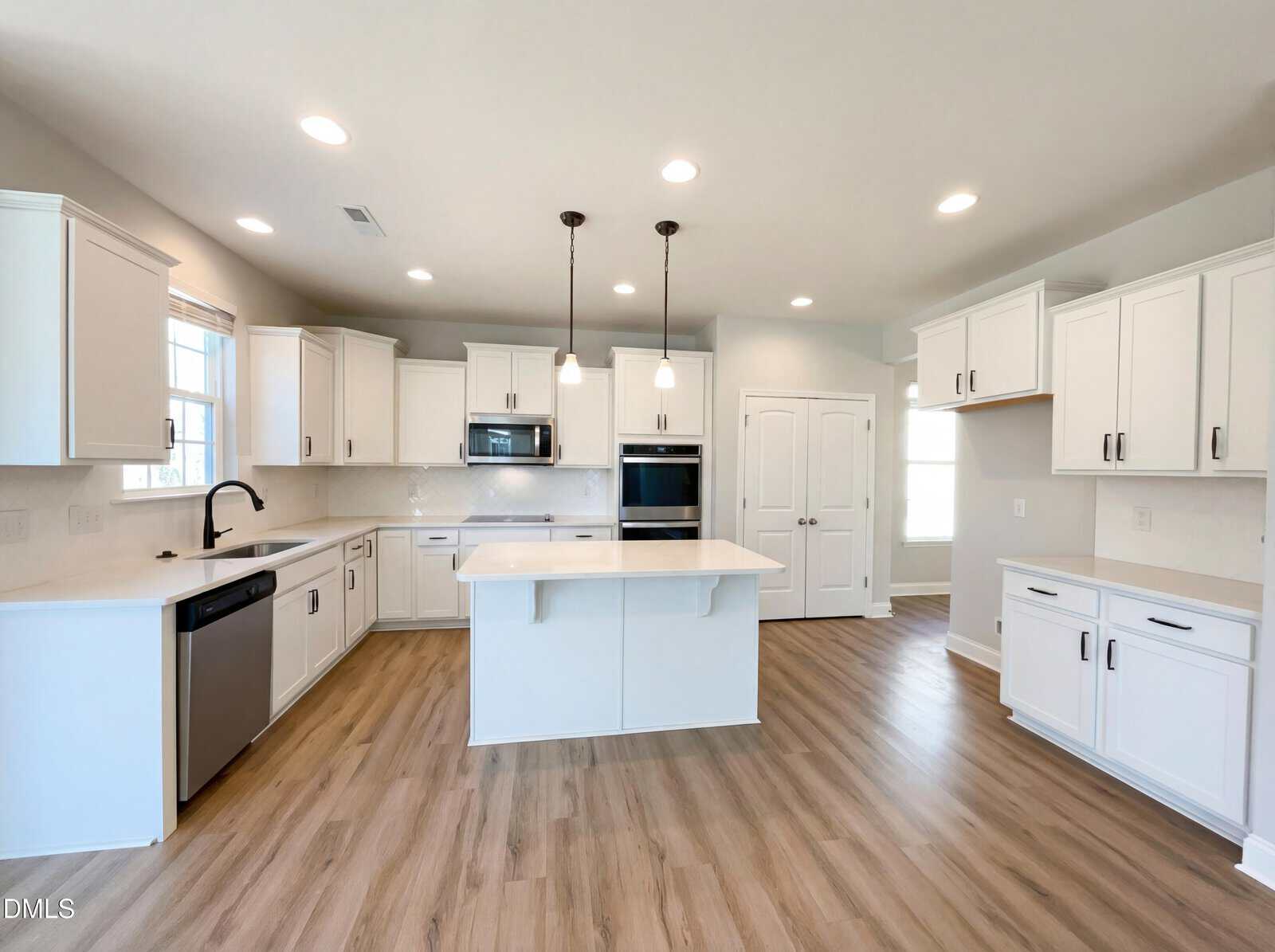 Modern kitchen with white cabinets, stainless steel appliances, center island with pendant lights, light wood flooring, and ample natural light from multiple windows.