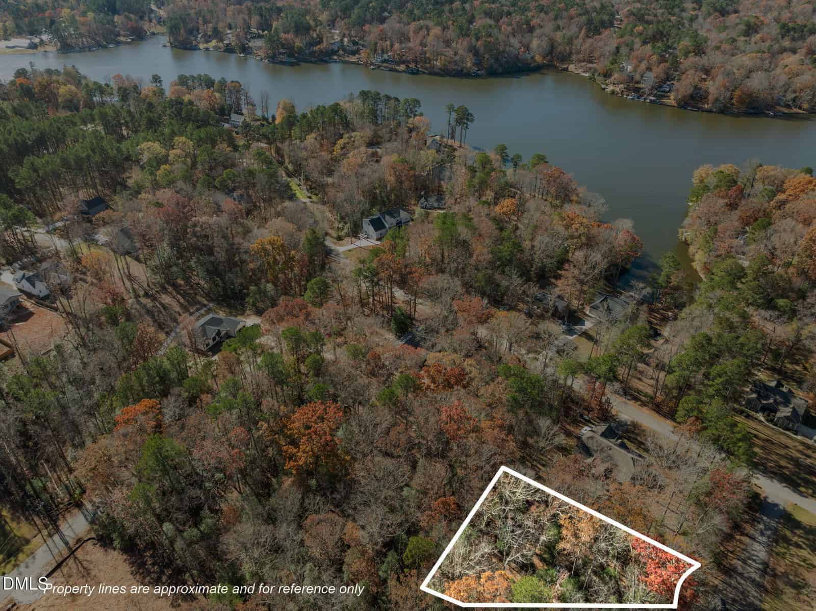 Aerial view of a wooded residential area near a lake, with a section of land outlined in white to indicate property boundaries. Several houses are scattered among the trees, and fall foliage covers the landscape.