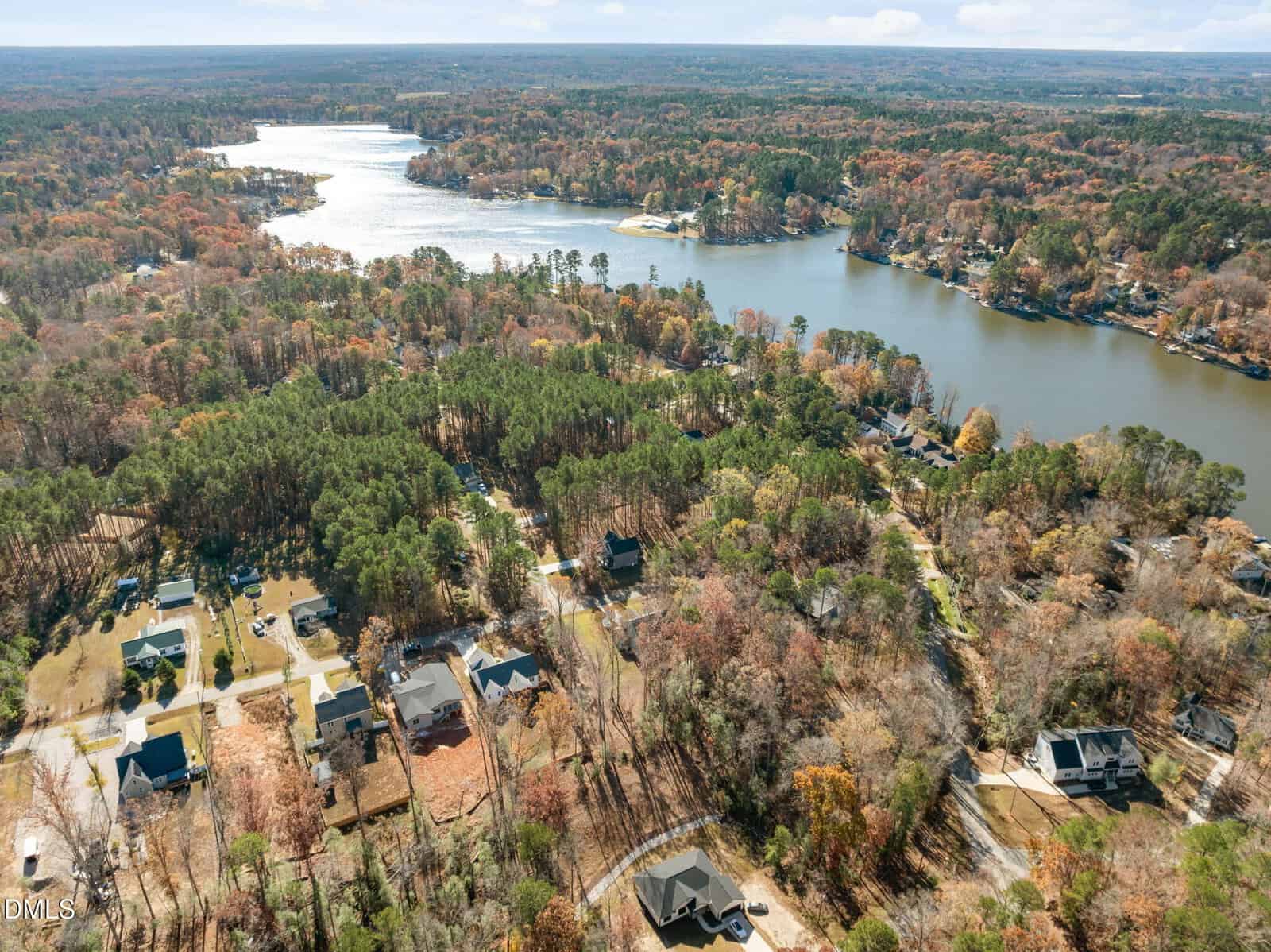 Aerial view of a wooded residential neighborhood near a large lake, with scattered houses, winding roads, and dense trees showing fall colors, all surrounded by forested land and water.