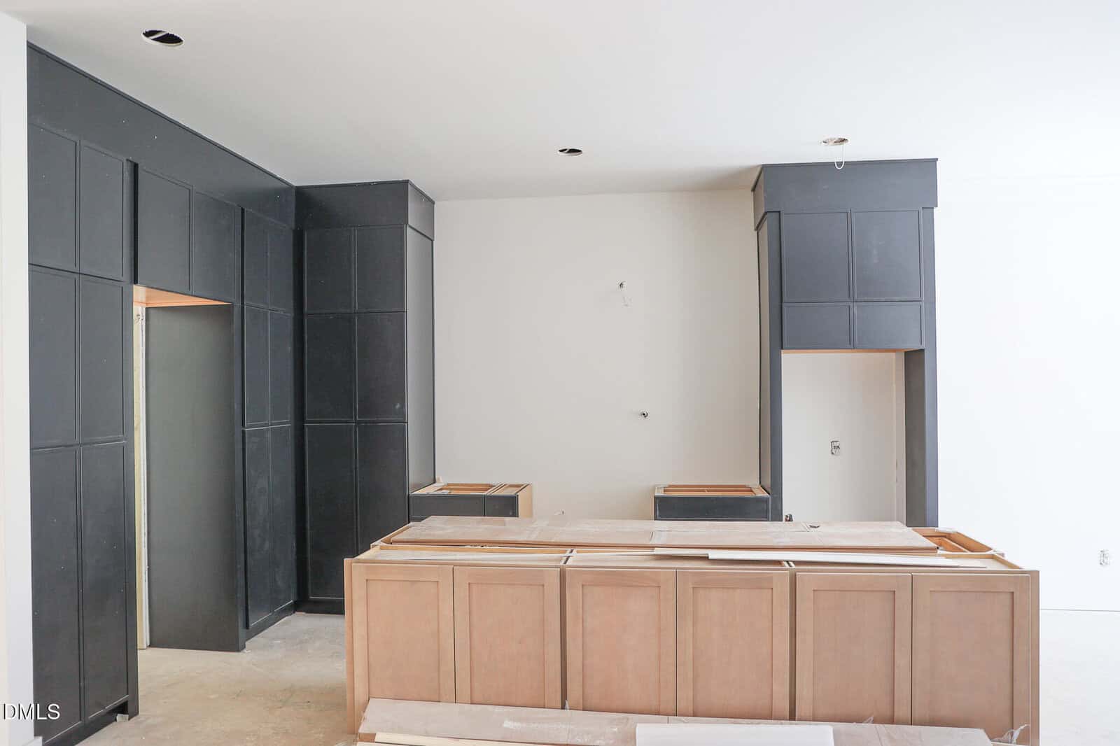 Unfinished kitchen with light wood lower cabinets and tall, dark upper cabinets. The counters are missing, and the floor appears incomplete, indicating the space is under construction or renovation.