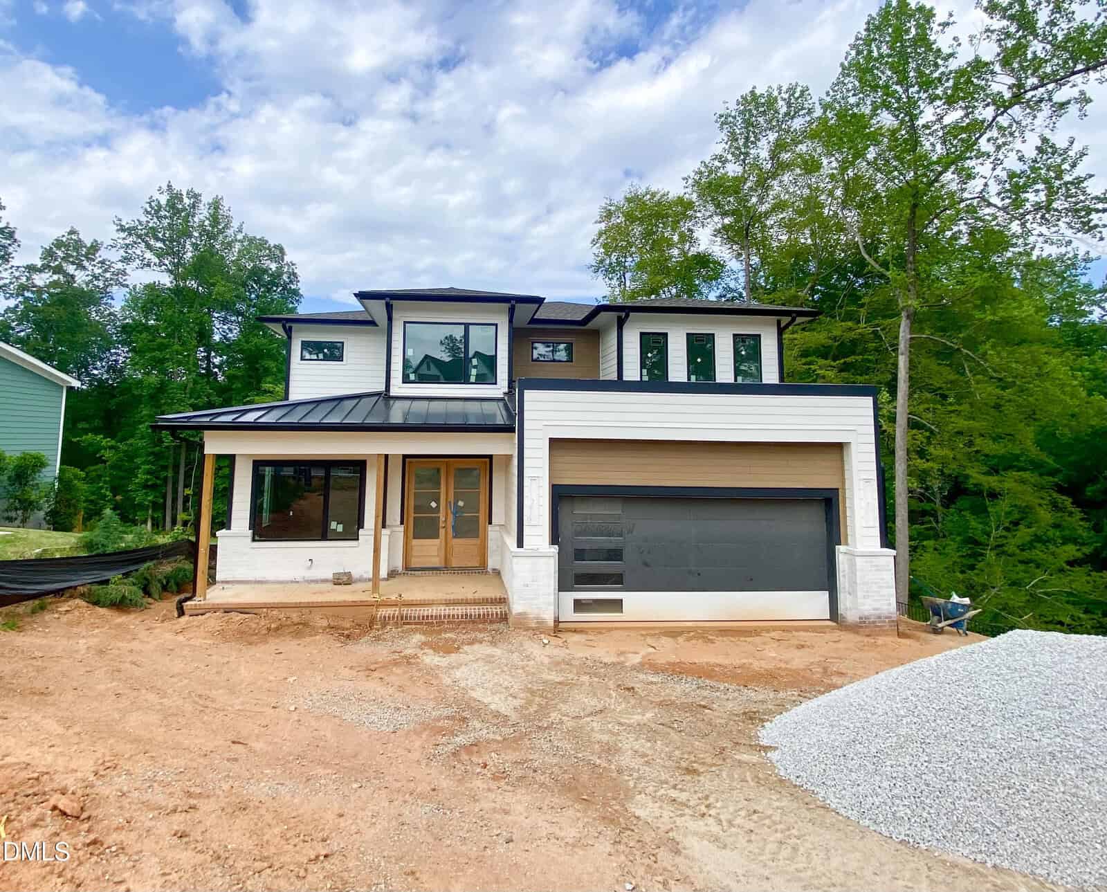 Modern two-story house at 209 Red Cardinal Court, Youngsville, with large windows, a covered porch, and double garage under construction. Surrounded by trees, the front yard features exposed soil and a pile of gravel.