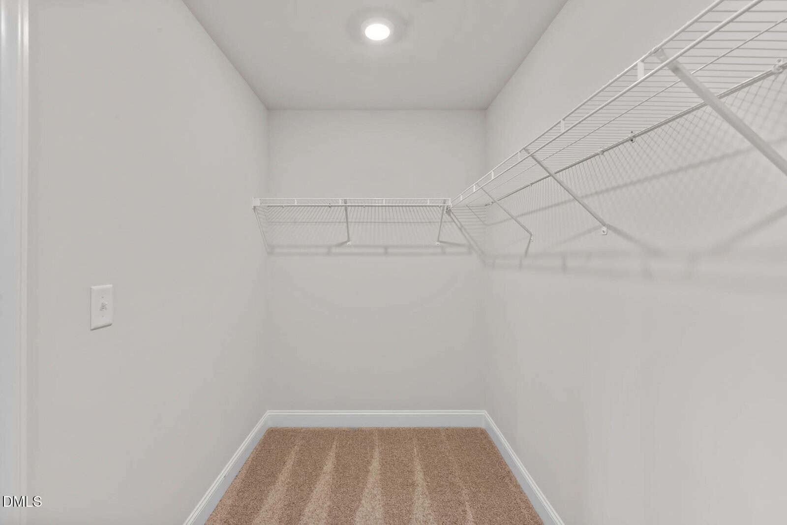 Empty walk-in closet with beige carpet, white wire shelving on two walls, white walls, and a ceiling light.