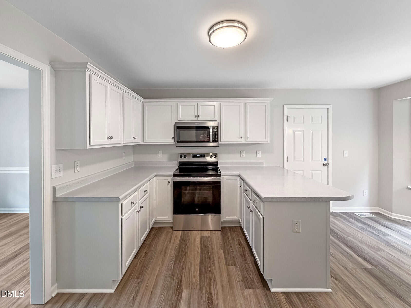 Modern kitchen with white cabinets, stainless steel appliances, electric stove, and microwave. The room features light gray walls and wood-style flooring, with ample countertop space and a ceiling-mounted light.