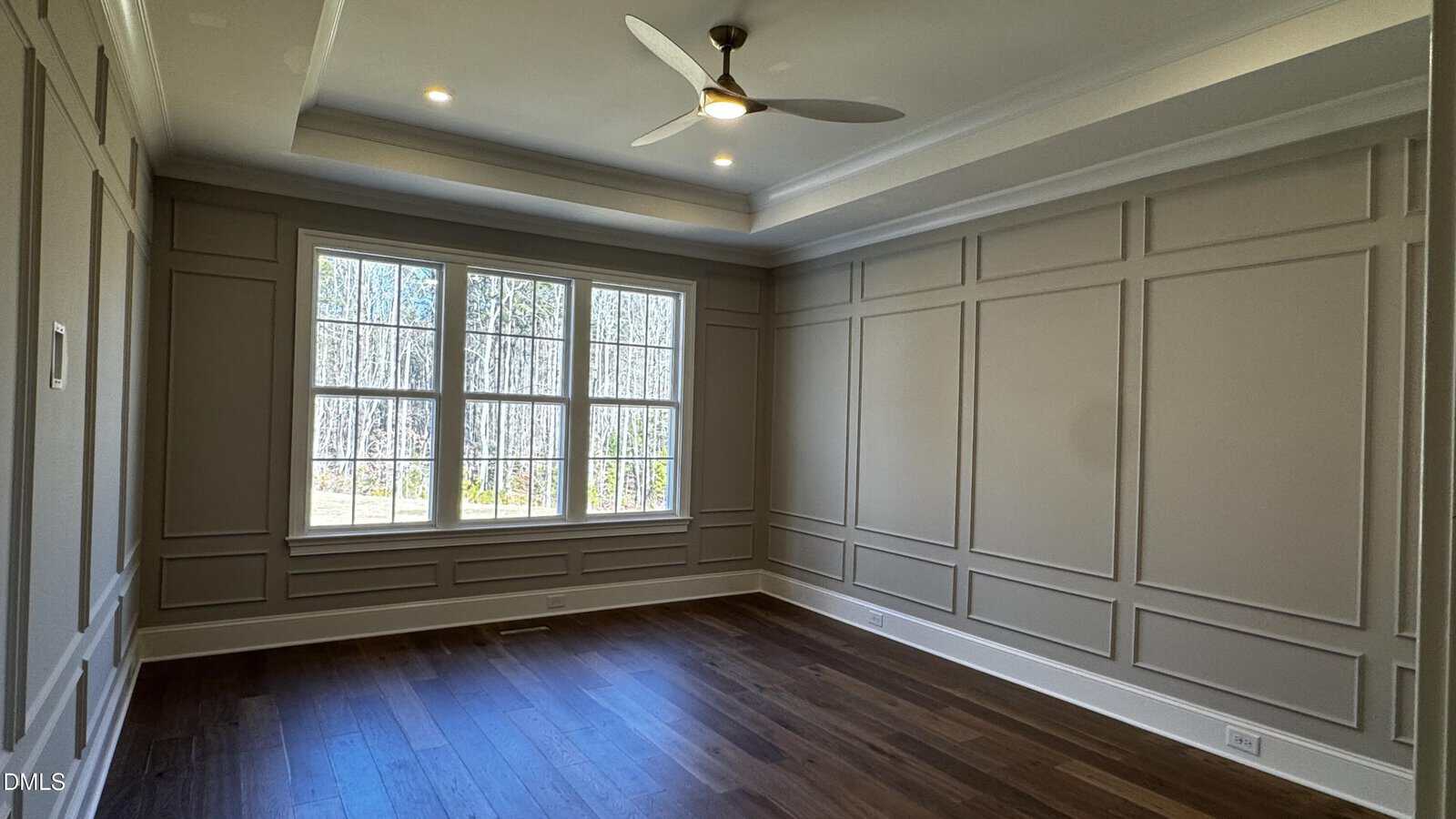 Empty room with light brown paneled walls, large windows letting in daylight, dark hardwood floors, a ceiling fan, and recessed lighting.