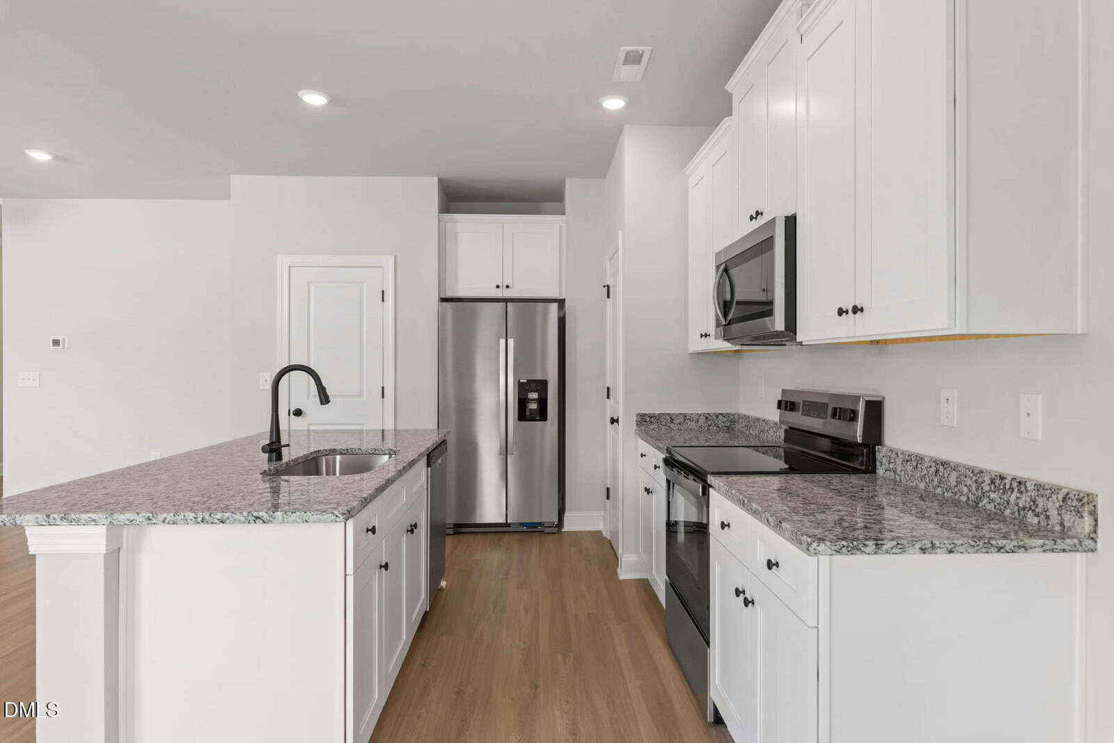 Modern kitchen with white cabinets, granite countertops, stainless steel appliances, an island with a sink and black faucet, and light wood flooring. The space is bright with recessed lighting.