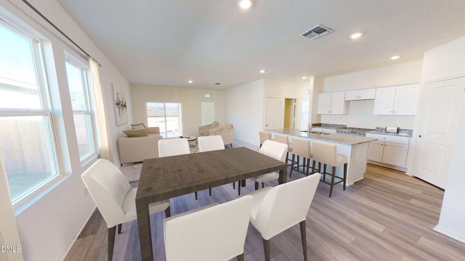 Modern open-plan dining and living area with white chairs, dark dining table, breakfast bar, white kitchen cabinets, large windows, and wood-style flooring. Neutral tones and spacious layout.