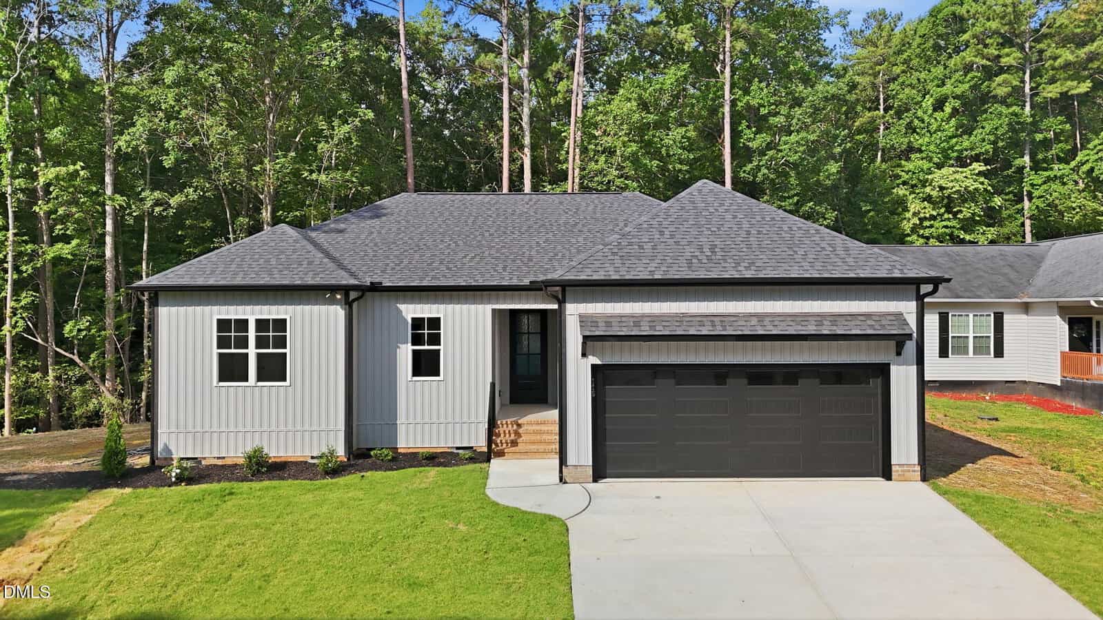 A modern single-story gray house at 116 Mohave Drive, Louisburg, with a dark gray roof, black trim, and double garage. Features a small front porch, steps to the door, green grass yard, and tall trees in the background.
