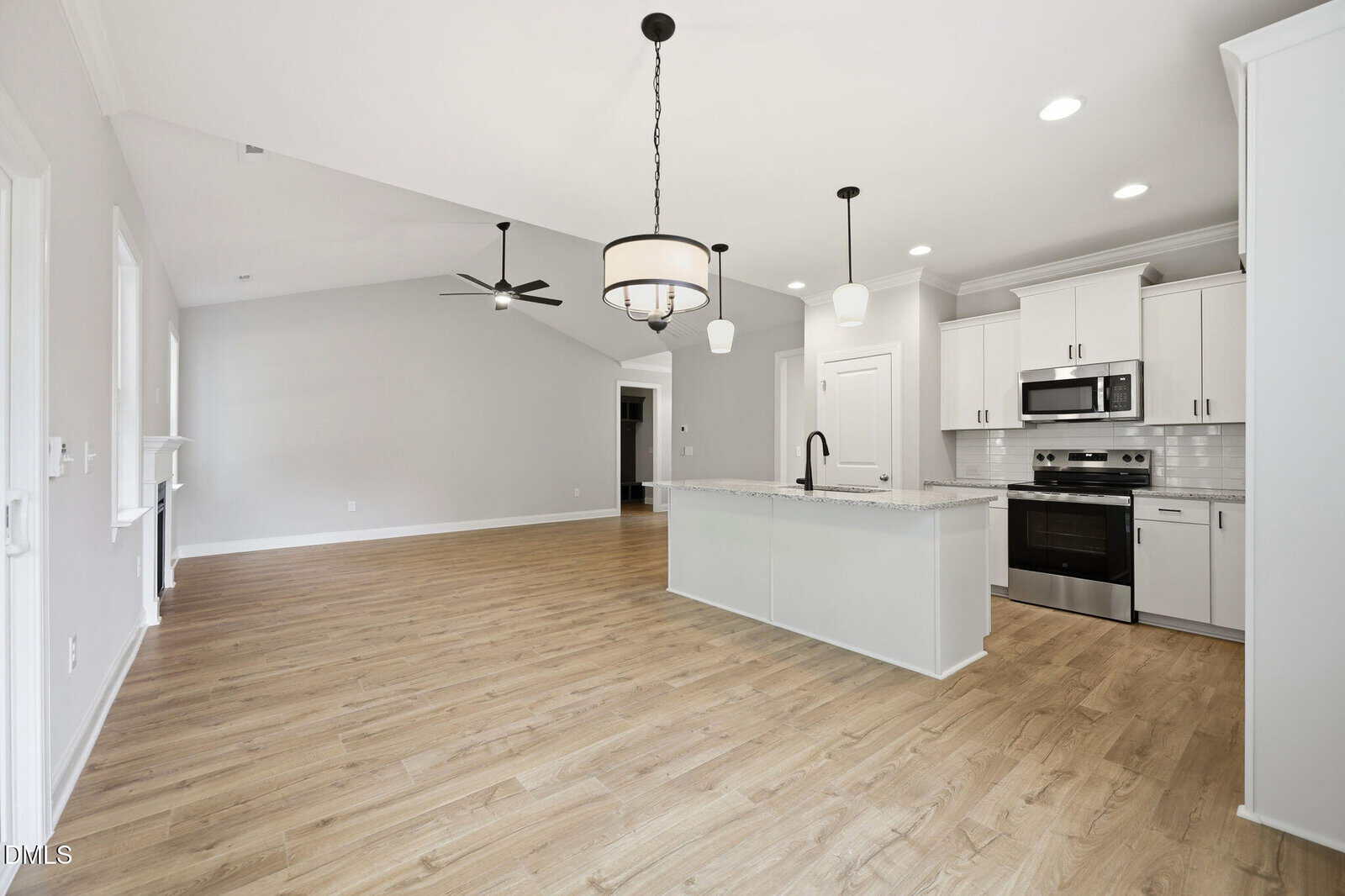 Open-concept kitchen and living area with light wood floors, white cabinets, stainless steel appliances, an island, pendant lighting, and a ceiling fan. Walls are light gray with white trim, creating a bright, airy space.