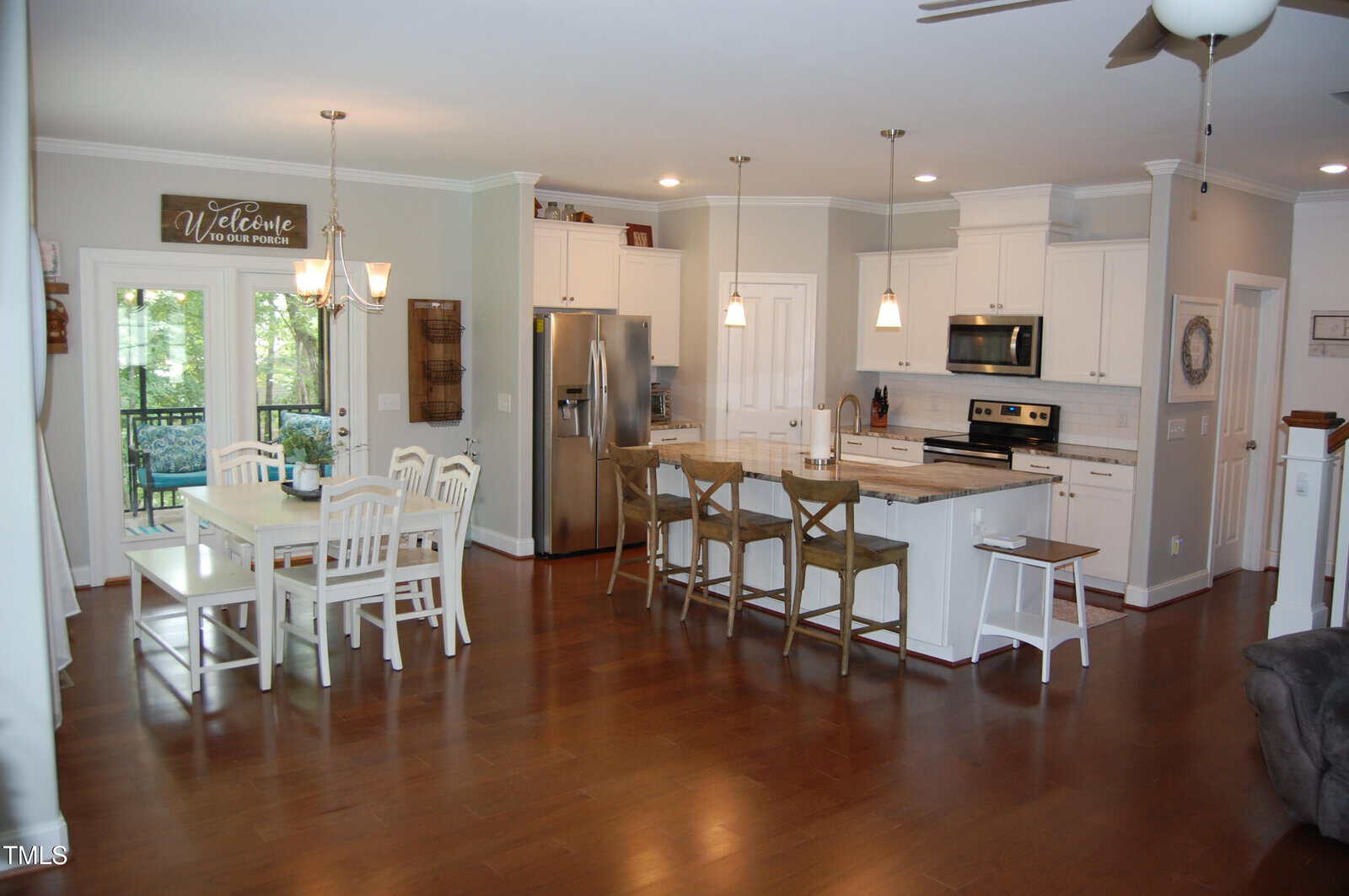 A spacious open-concept kitchen and dining area with white cabinets, stainless steel appliances, a center island with stools, a dining table with chairs, pendant lighting, and hardwood floors.