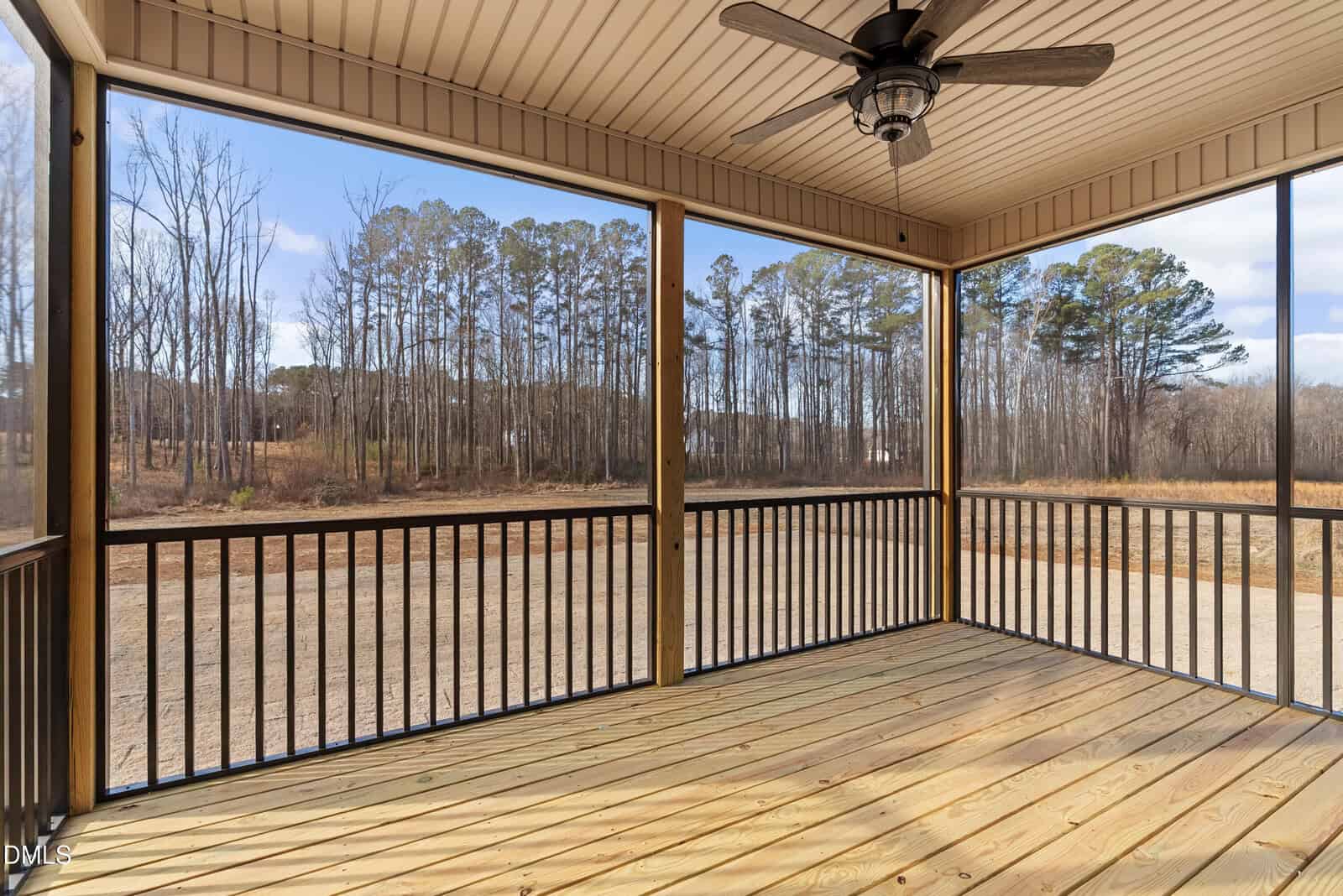 A screened-in porch with a ceiling fan and wooden floor overlooks a natural landscape with bare trees and clear skies in the background.