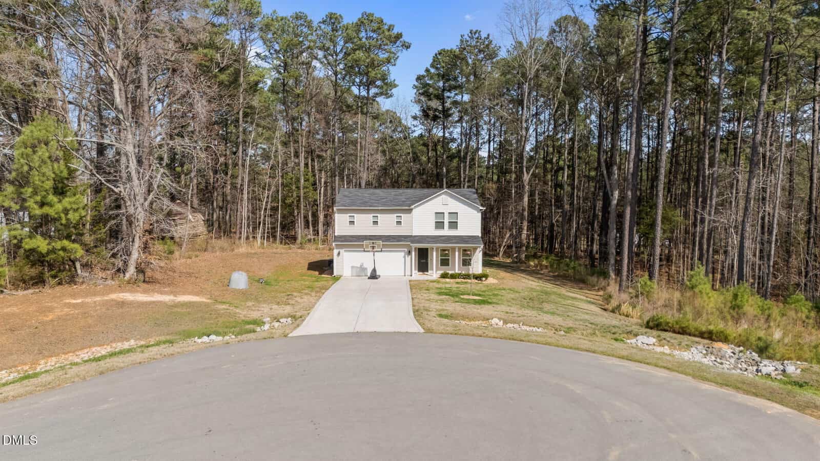 A two-story white house with a covered front porch sits at the end of a cul-de-sac, surrounded by pine trees and a large yard under a clear blue sky.