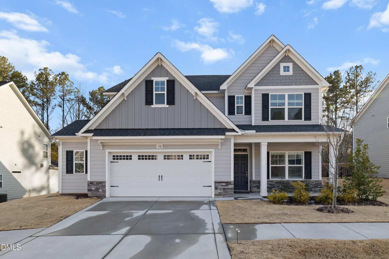 Two-story suburban house with gray siding, white trim, and black shutters situated at 110 Vast View Way in Youngsville. Features a double garage, front porch, and a neatly maintained lawn with small shrubs. Sky is clear with a few clouds.