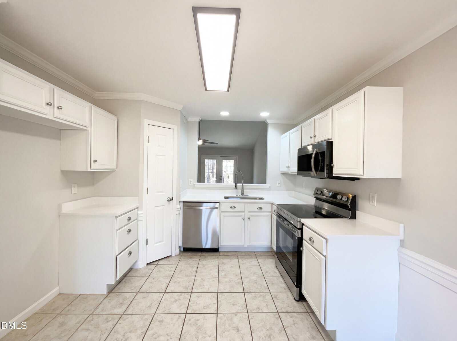 Modern kitchen with white cabinets, stainless steel appliances, a built-in microwave, and a tile floor. There is a pantry door, under-cabinet lighting, and a rectangular ceiling light fixture.
